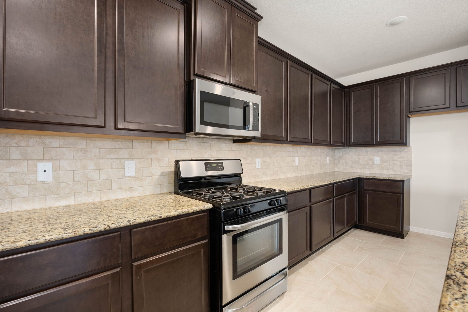23643 Balzano Court, Katy, TX 77493 Warm and inviting culinary haven featuring expansive earth-toned granite countertops, continuous premium espresso cabinetry, and sleek integrated stainless steel appliances.