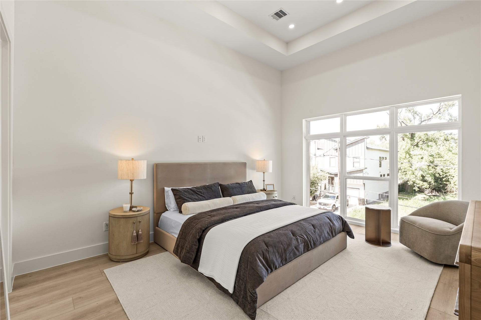 The primary bedroom. Tray ceiling, a full wall of windows over the street, and room for a king plus a sitting chair.