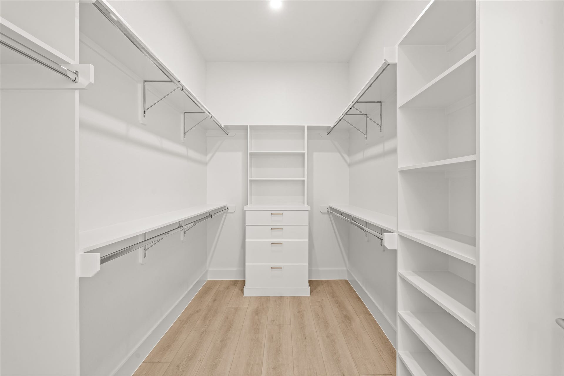 Primary walk-in closet with double hanging rods, built-in shelving, and a center dresser. Room for two wardrobes, honestly.