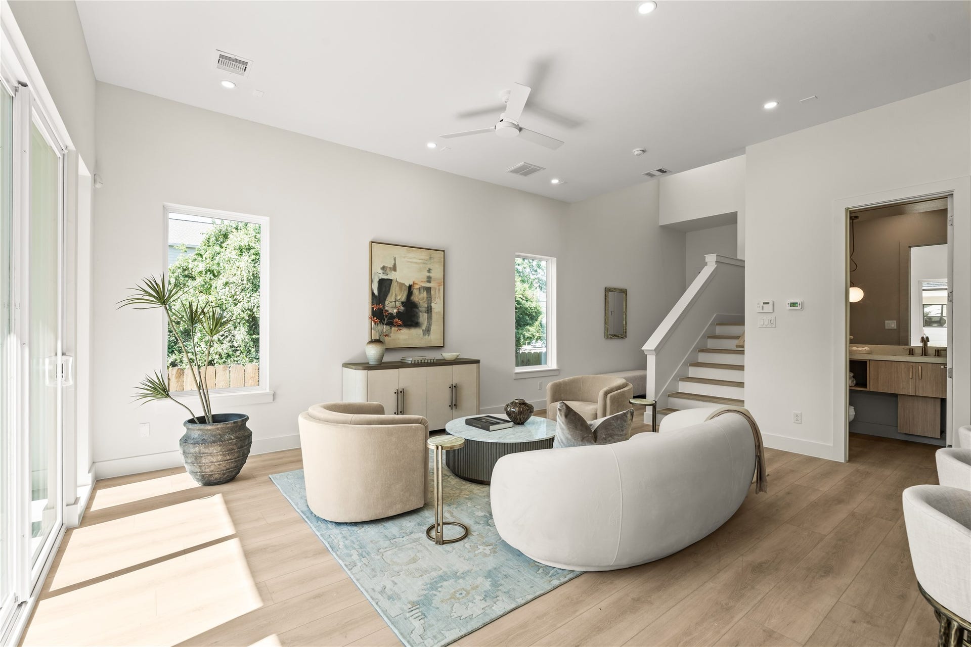 The stair run frames one side of the living room, with the primary suite entry just past it. Wide-plank vinyl floors carry through the whole first floor.