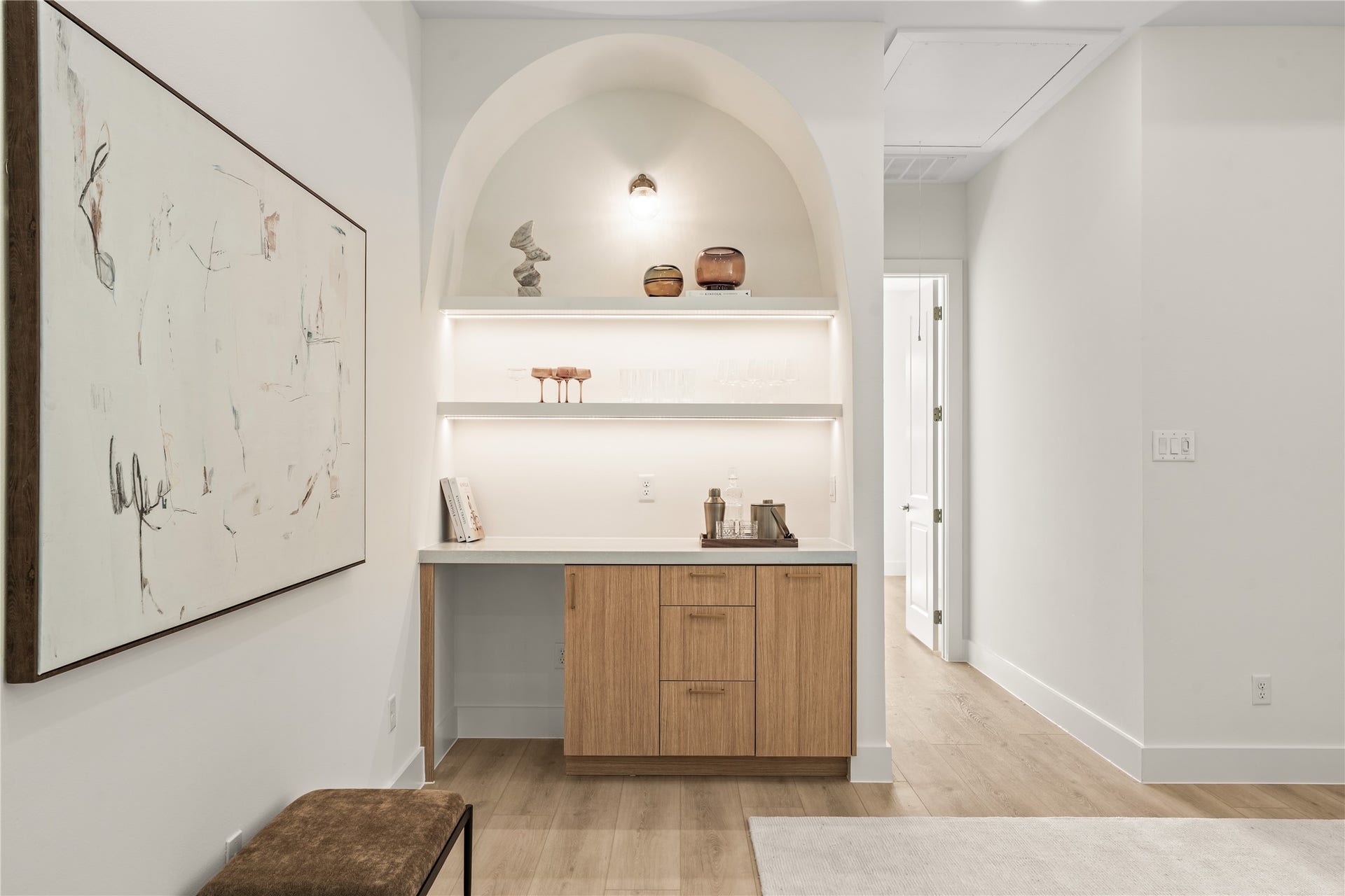 The dry bar up close. Arched niche, under-lit shelving, quartz counter, and wood cabinets below for the bottles.