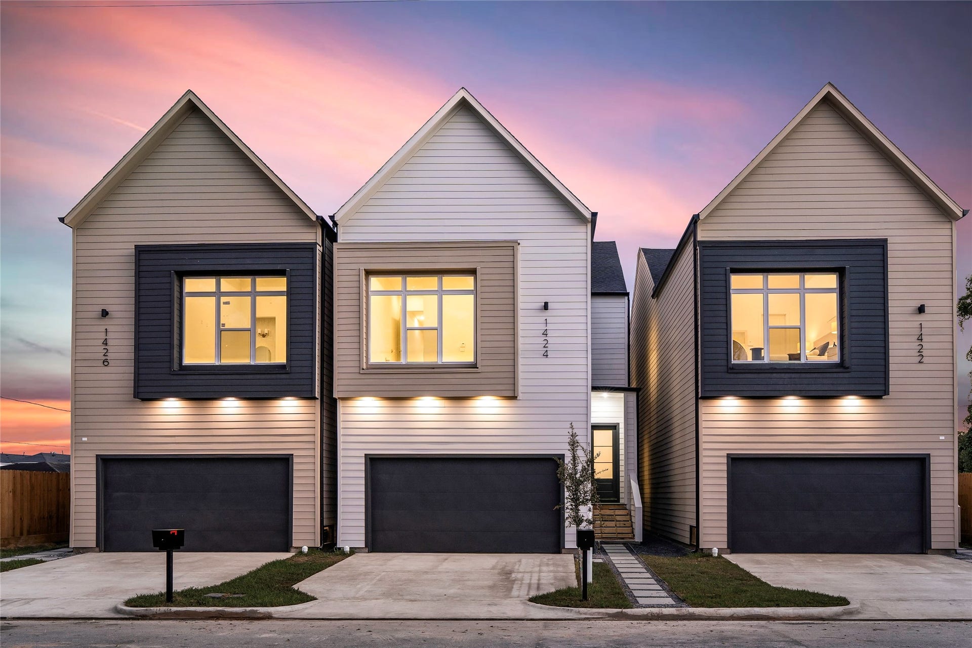 This one is the white elevation. Crisp white siding with a warm tan window surround, a dark garage door, and uplighting under the eaves. Clean lines, no clutter, and it reads even better at dusk with the lights on.