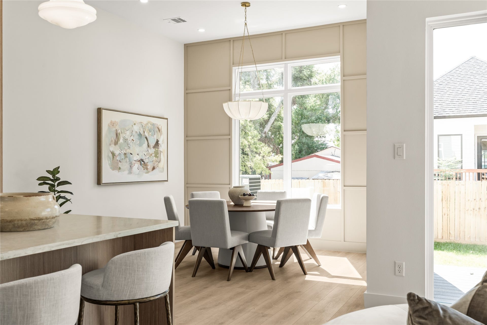 Dining off the kitchen with a wood-paneled accent wall and a tall window over the table. The yard sits just outside, so dinner comes with a view.