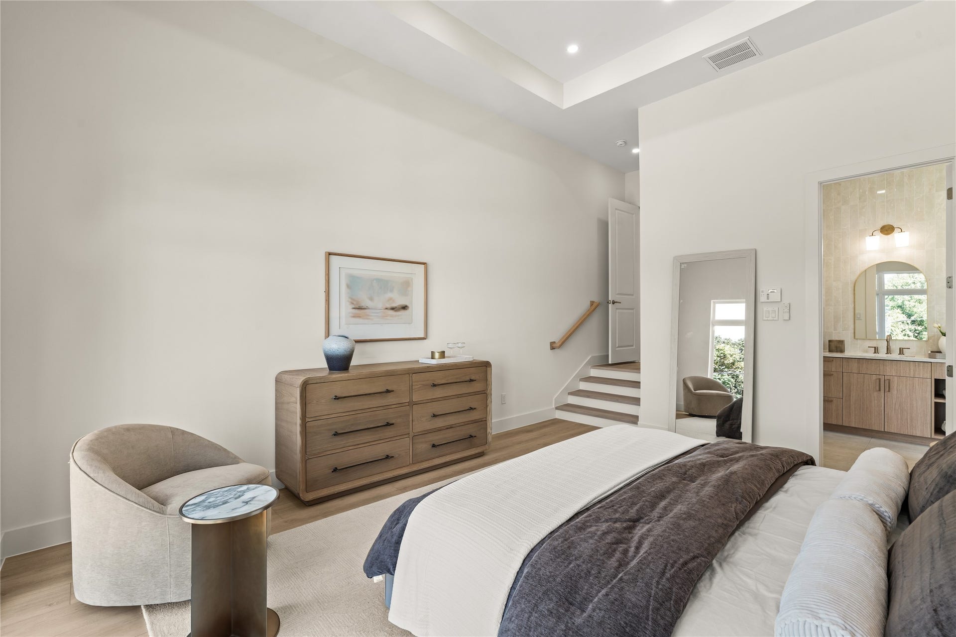 Primary suite from the bedside. The bath and the walk-in closet sit just past the dresser, through the double doors.
