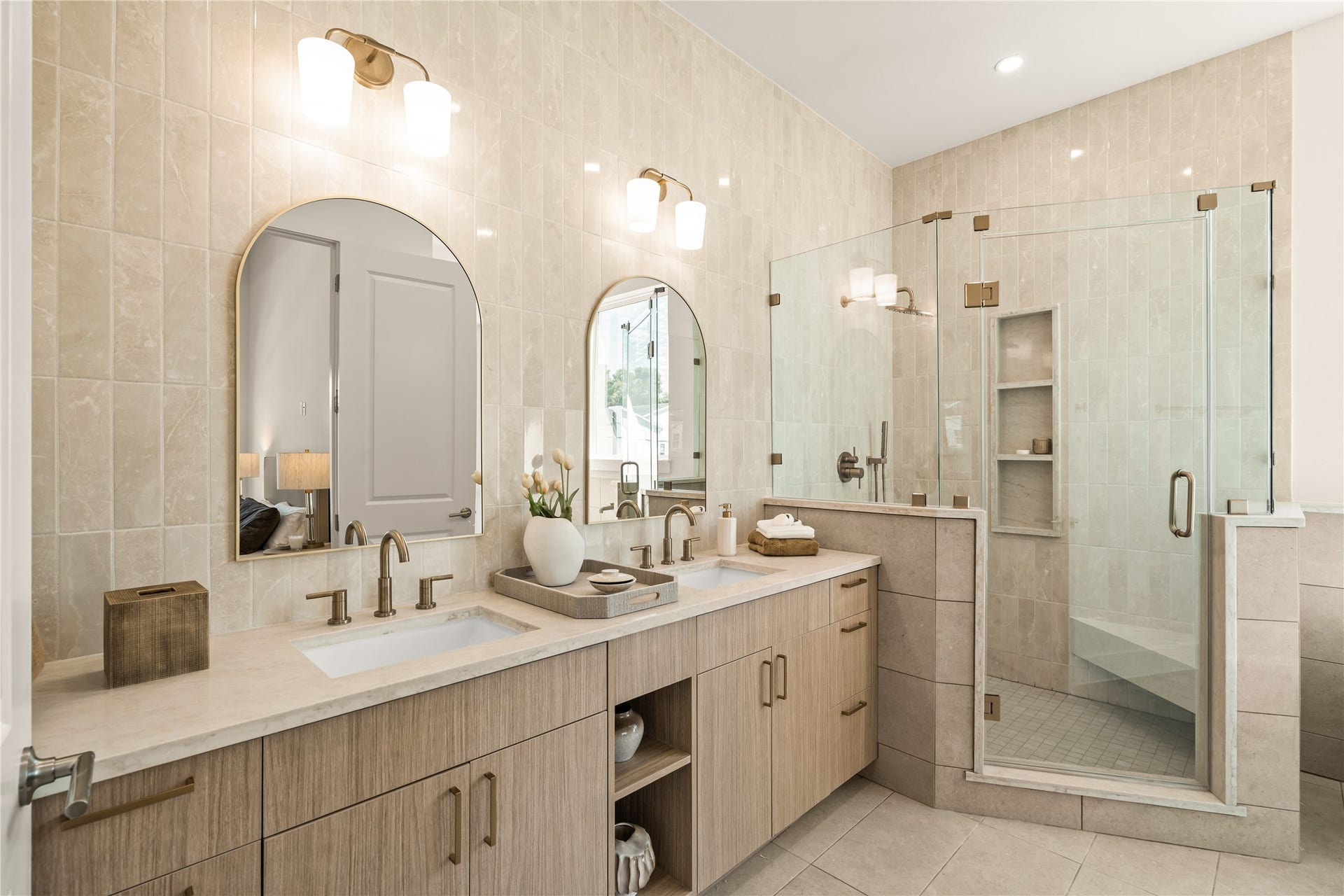 Primary bath from the doorway. Frameless glass shower with a built-in bench, a niche for bottles, and brass fixtures against the tile.