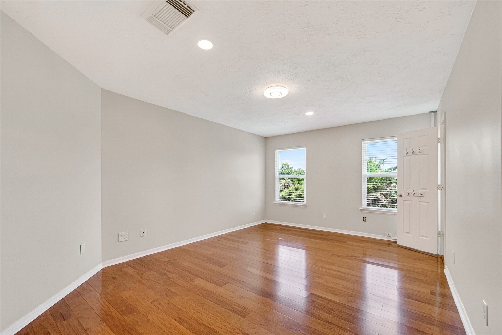 Bright and spacious room featuring polished wood floors, recessed lighting, and large windows that invite natural light.