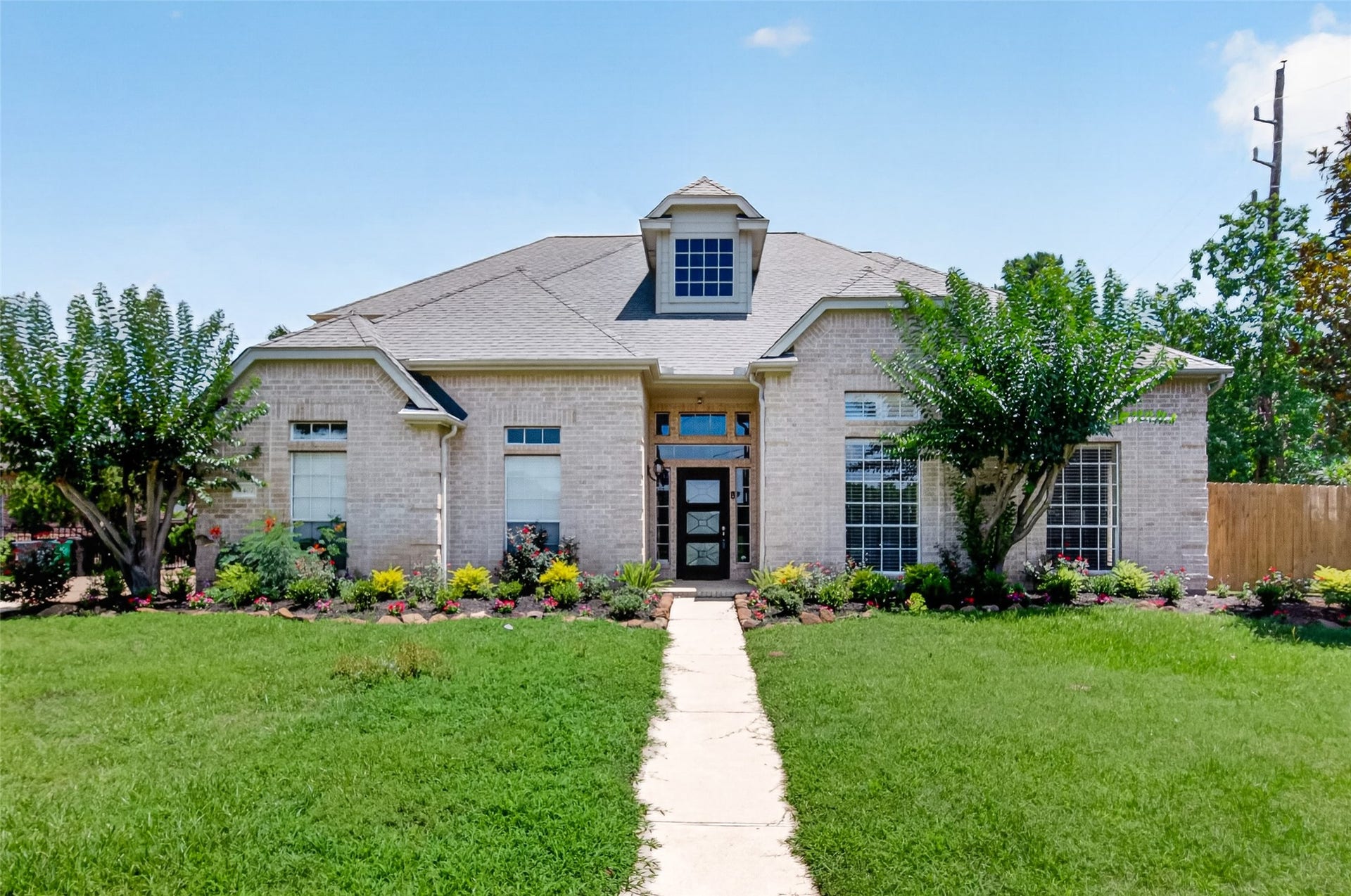 Charming single-story brick home with a welcoming front porch, surrounded by lush landscaping and mature trees.