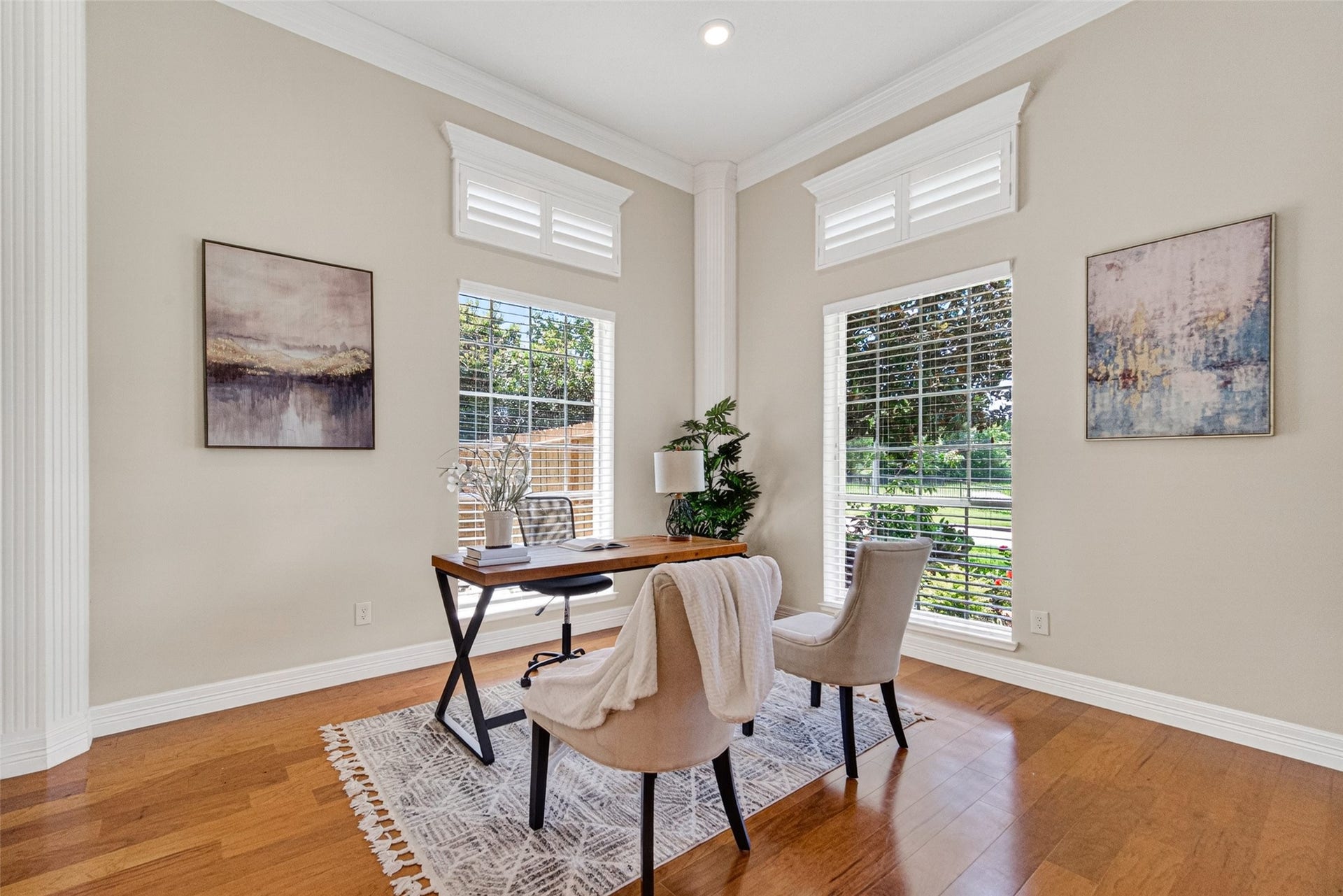 Bright and inviting home office features large windows with plantation shutters, elegant hardwood floors.