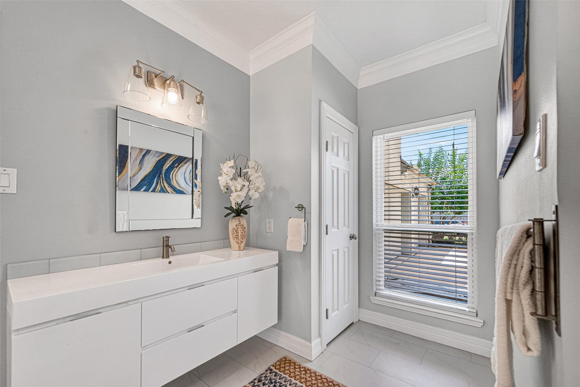 Bright and modern primary bathroom featuring a sleek white vanity with ample storage, elegant lighting, and a large window that fills the space with natural light.