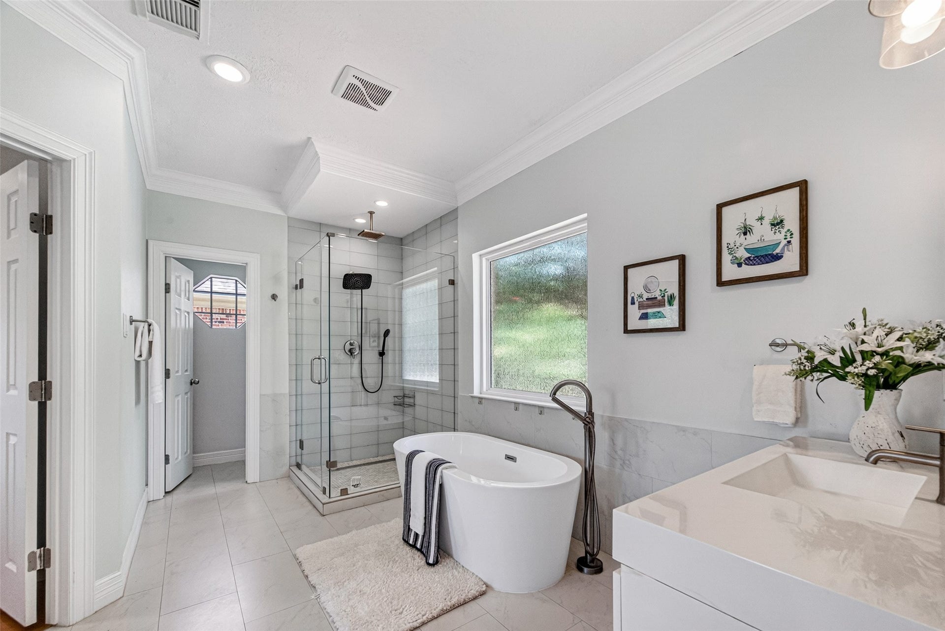 This primary bathroom features a modern design with a large glass-enclosed shower, a standalone bathtub, and a sleek vanity. The space is bright and airy, with neutral tones and stylish decor, creating a relaxing atmosphere.