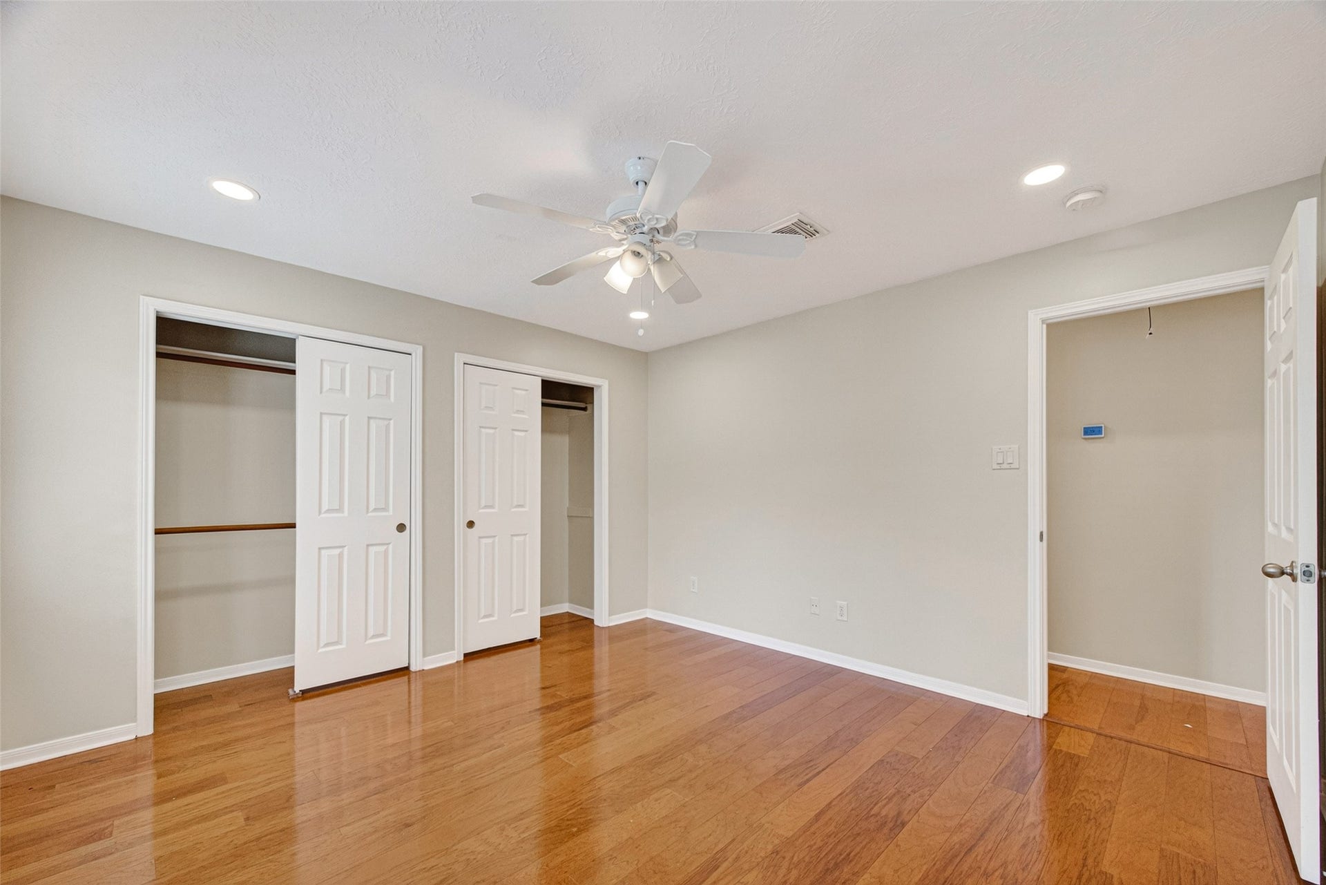 Spacious bedroom featuring polished wood floors, dual closets with sliding doors, and a ceiling fan for comfort.