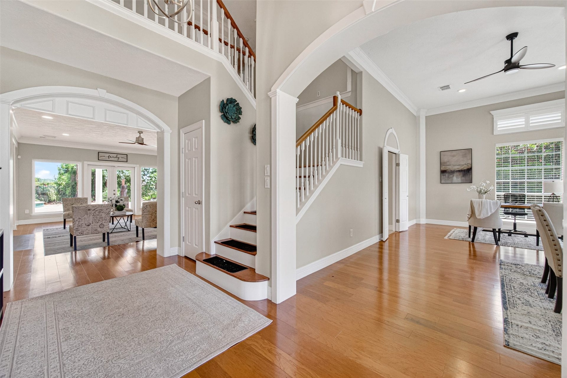 Step into a grand entryway with elegant wood flooring, soaring ceilings, and an open layout that seamlessly flows into a sunlit living and dining area,