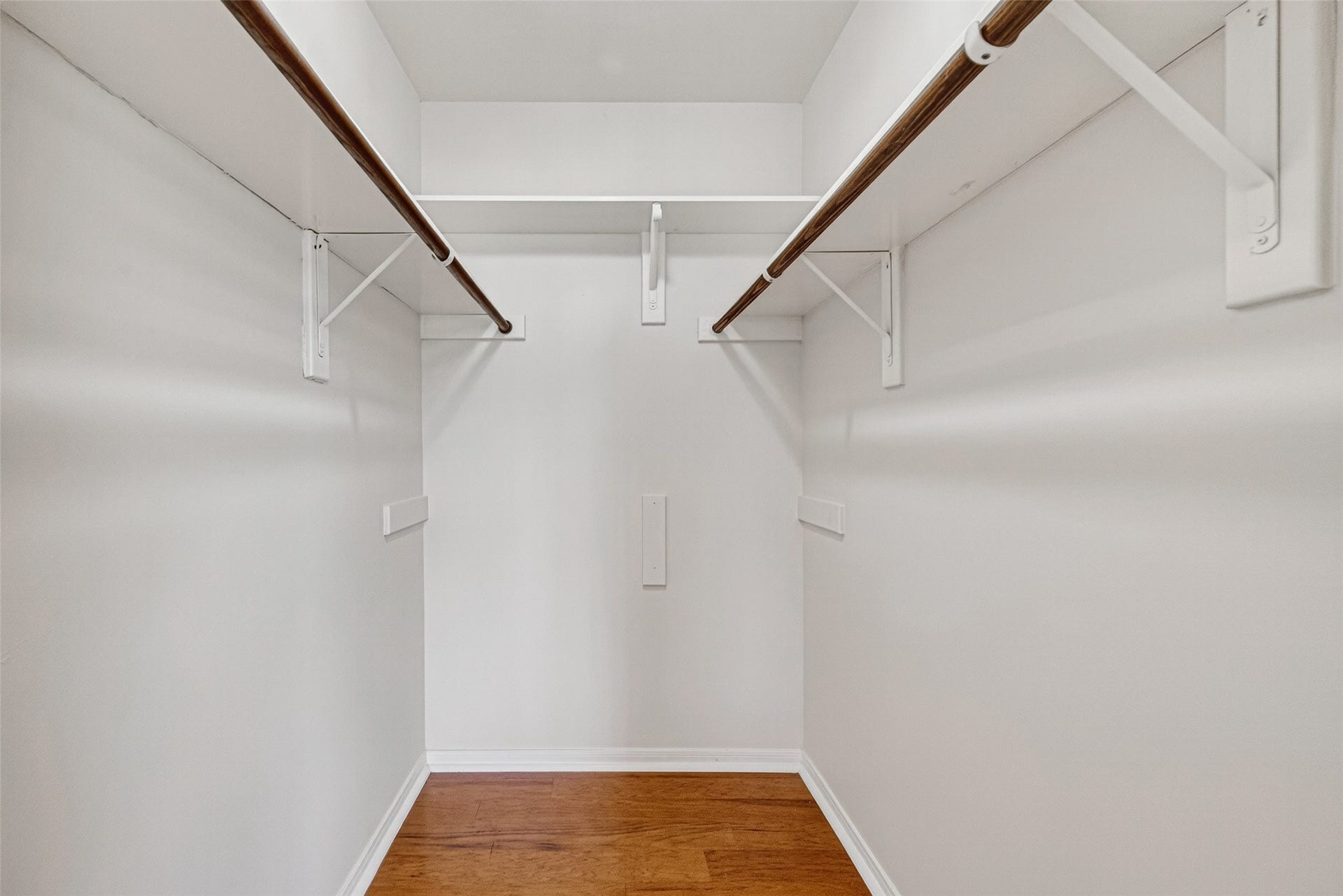 Spacious walk-in closet with dual hanging rods and sleek wooden flooring, perfect for organized storage.