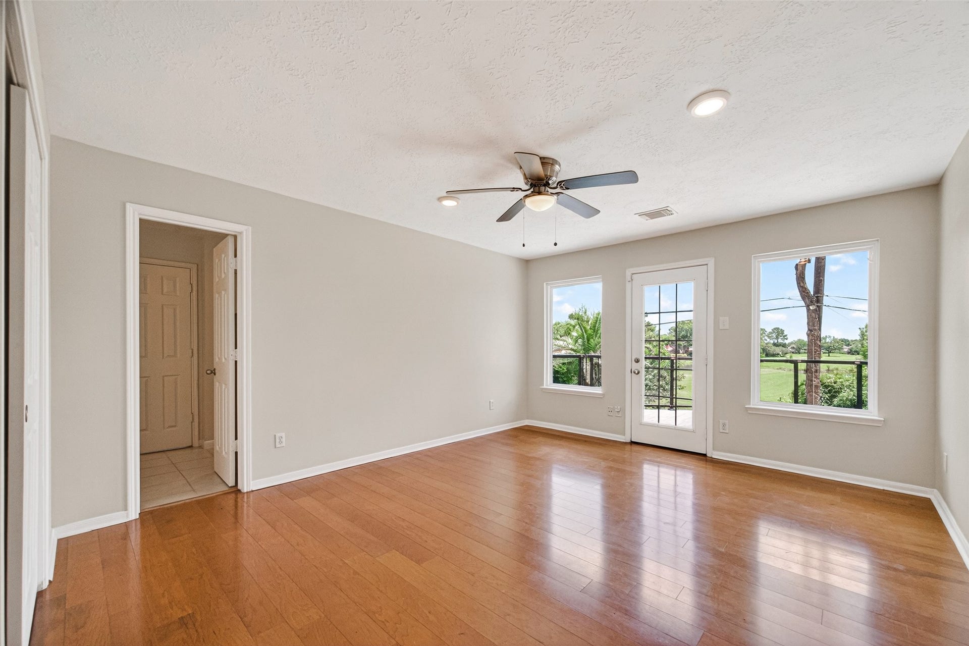 A bright and spacious bedroom with gleaming wood floors, a ceiling fan for comfort, and large windows that frame stunning golf course views.