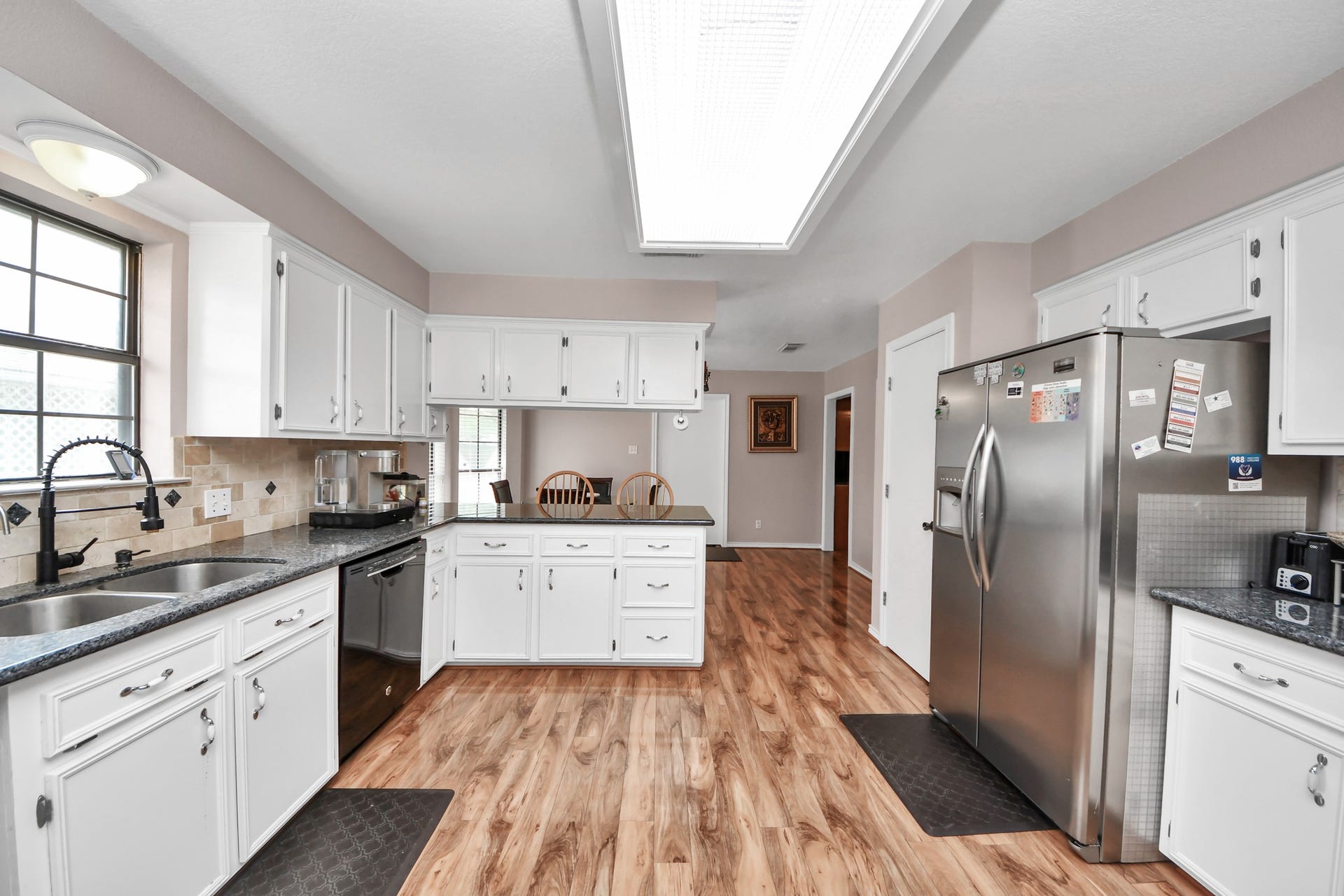 12746 Roy Road, Pearland, TX 77581 This kitchen features white cabinetry, granite countertops, and stainless steel appliances. It has wood-style flooring, a double sink, and a large window for natural light. The layout is spacious and functional for cooking and entertaining.