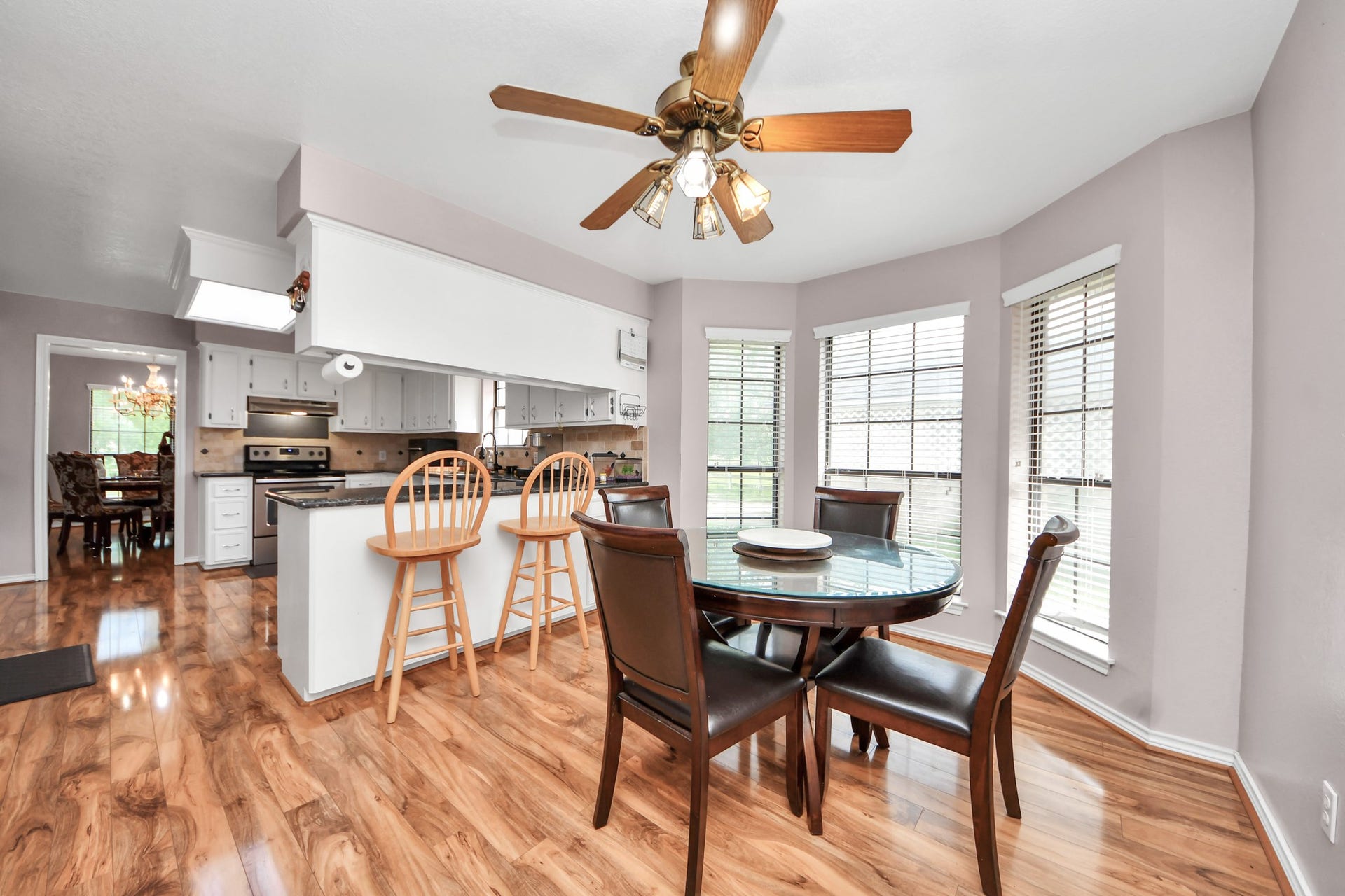 12746 Roy Road, Pearland, TX 77581 Bright and airy kitchen with a central island and bar seating, open to a cozy dining area with large windows. The space features hardwood floors, stainless steel appliances, white cabinetry, and a ceiling fan.