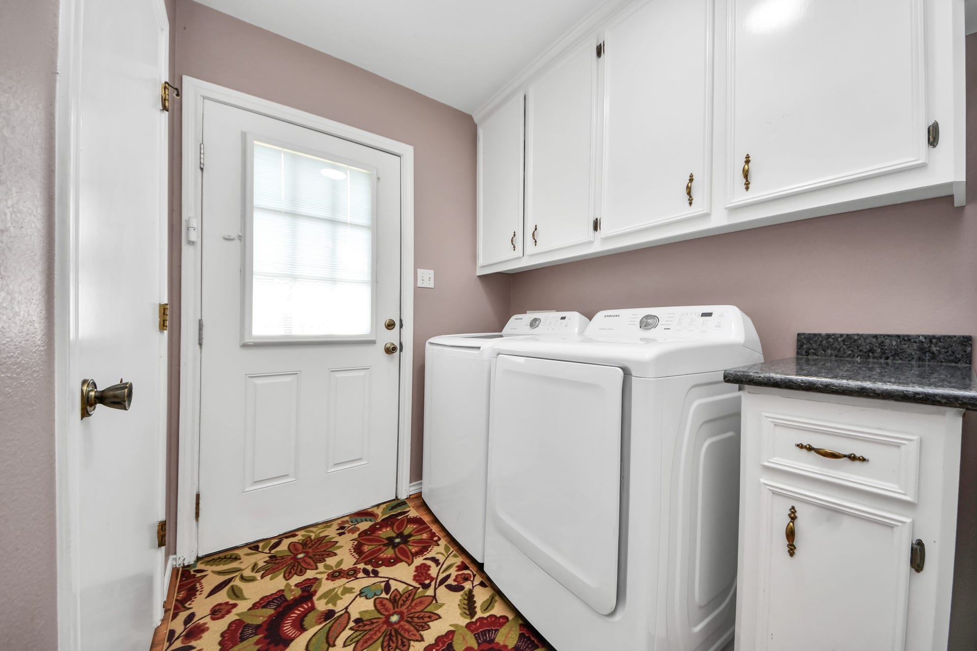 12746 Roy Road, Pearland, TX 77581 This photo showcases a tidy laundry room featuring a washer and dryer, white cabinetry for storage, and a decorative floral rug. The room has a door with a window, allowing natural light to enter, and a countertop for added convenience.
