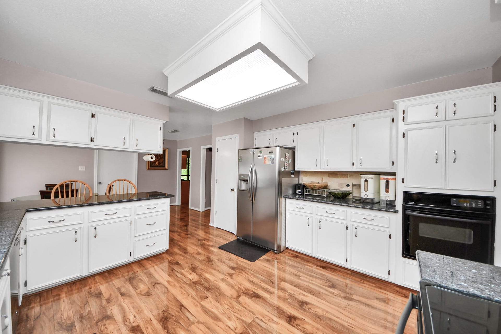 12746 Roy Road, Pearland, TX 77581 This kitchen features ample white cabinetry, granite countertops, and stainless steel appliances, including a double-door fridge. The space is well-lit with a central ceiling light, and the hardwood floors add warmth. There's a breakfast bar with seating, offering a cozy dining option.