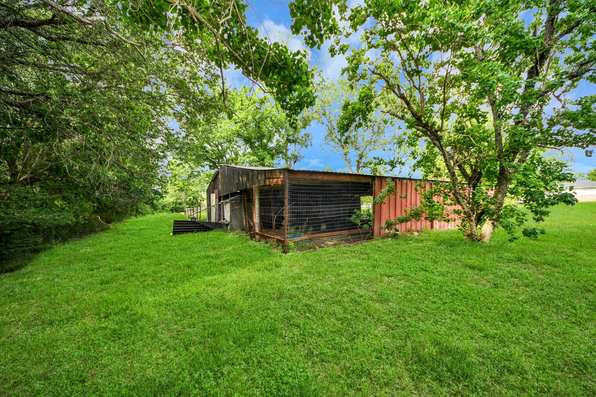 12746 Roy Road, Pearland, TX 77581 This photo features a rustic outdoor structure, possibly a small barn or storage shed, surrounded by lush green grass and mature trees, offering a natural, serene setting.