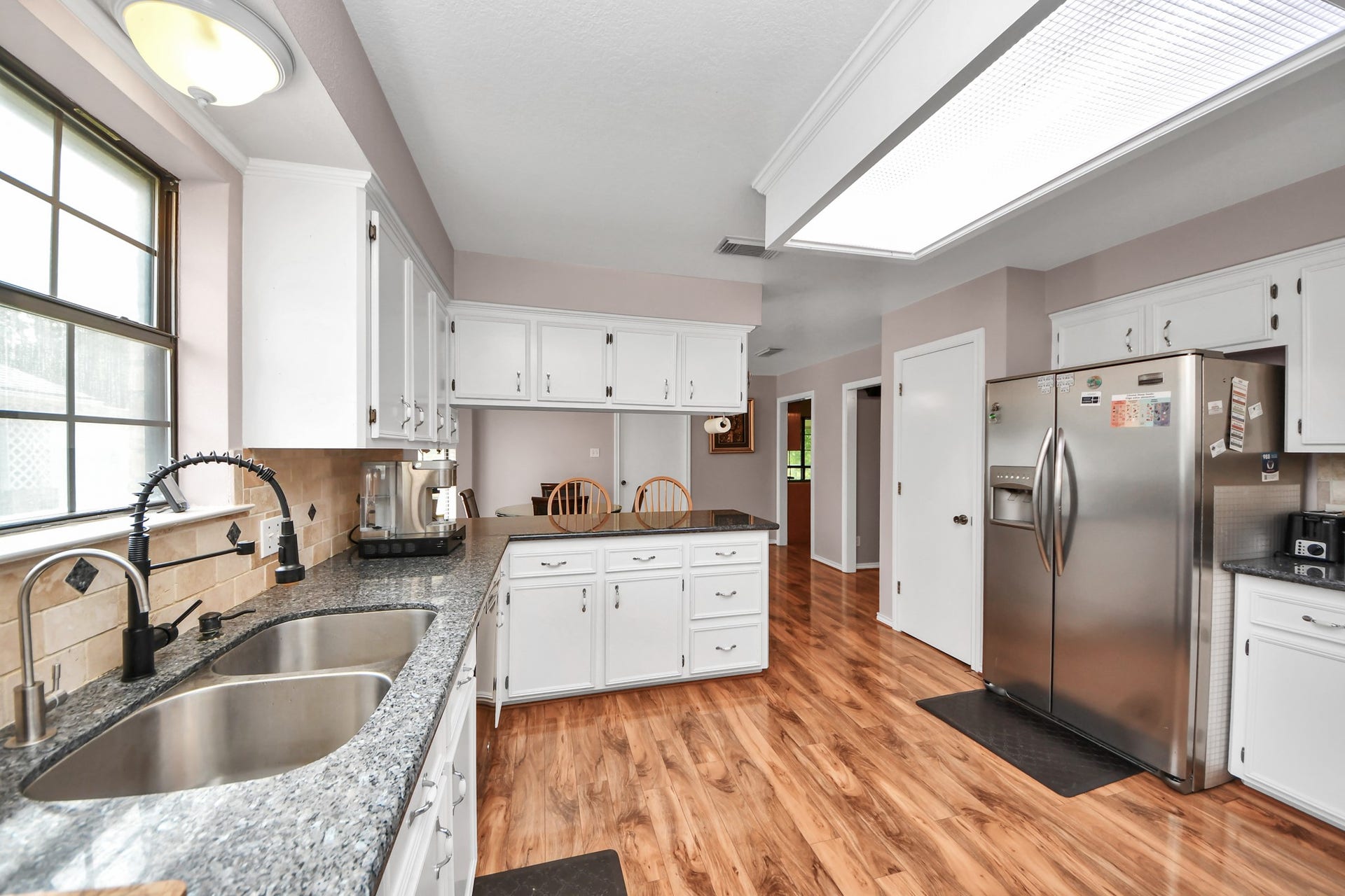 12746 Roy Road, Pearland, TX 77581 Bright and spacious kitchen featuring granite countertops, stainless steel appliances, and ample white cabinetry. The room is accented with wood flooring and a large window for natural light.