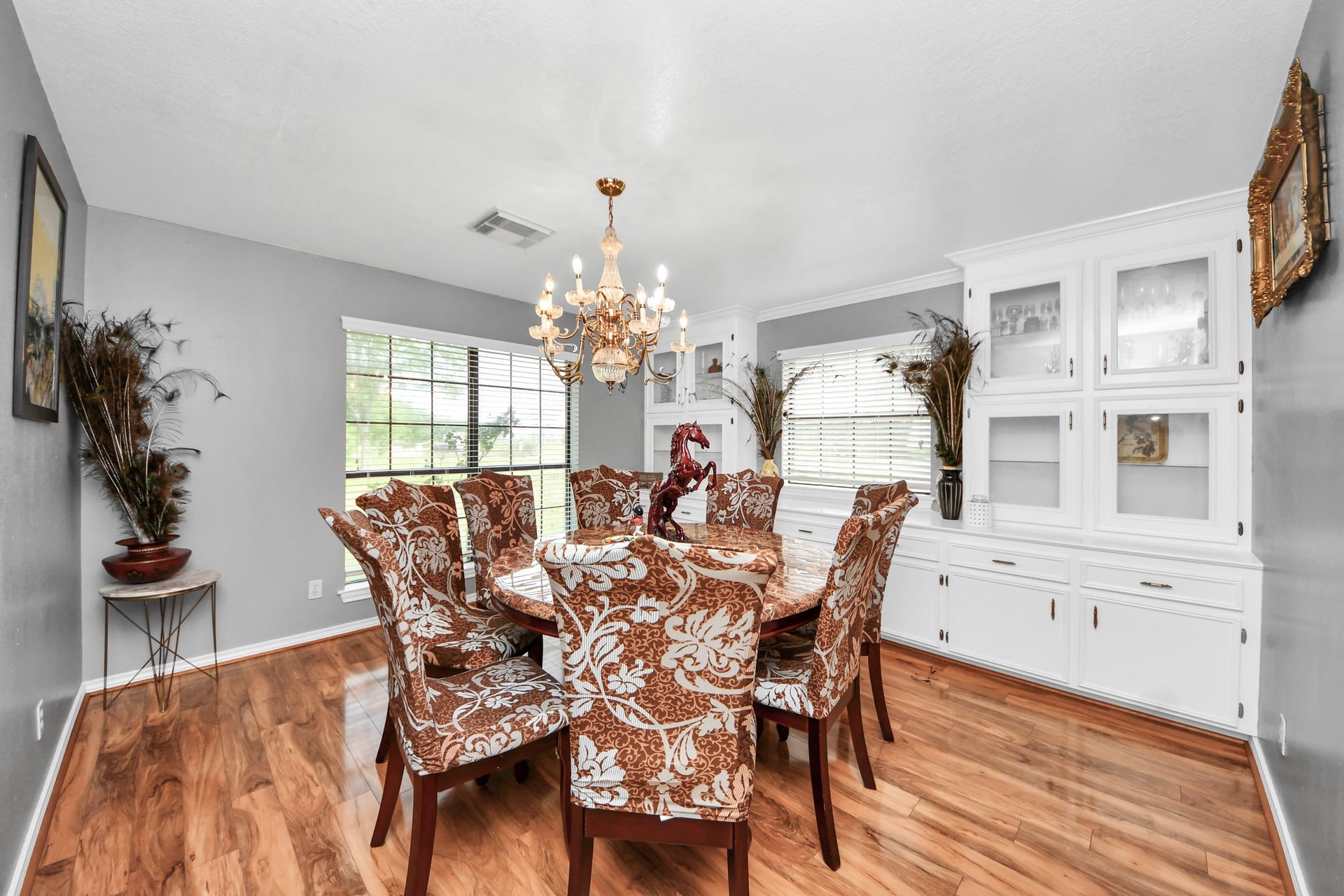 12746 Roy Road, Pearland, TX 77581 This dining room features elegant wood flooring, a large window for natural light, and a classic chandelier. It includes built-in white cabinetry and a spacious dining table with upholstered chairs, offering both style and functionality.