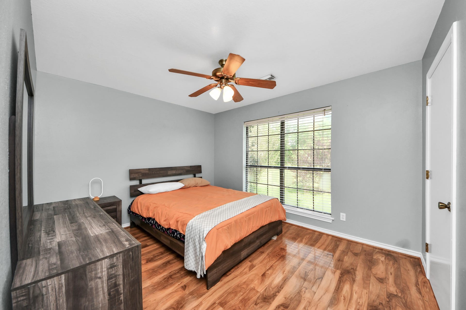 12746 Roy Road, Pearland, TX 77581 This bedroom features a cozy space with laminate wood flooring, a ceiling fan, and a large window for natural light. It includes a wooden bed frame, matching dresser, and neutral wall colors for a modern touch.