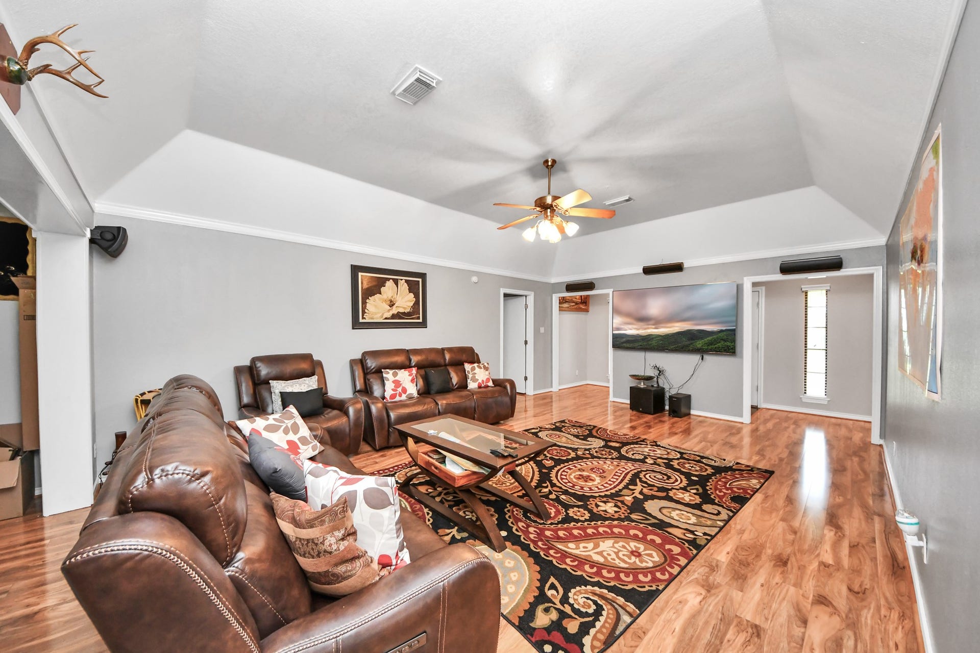 12746 Roy Road, Pearland, TX 77581 Spacious living room with high ceilings and wood flooring, featuring cozy leather sofas and a large TV. The room is brightened by a ceiling fan with lights and has tasteful wall art and a patterned area rug for added warmth.