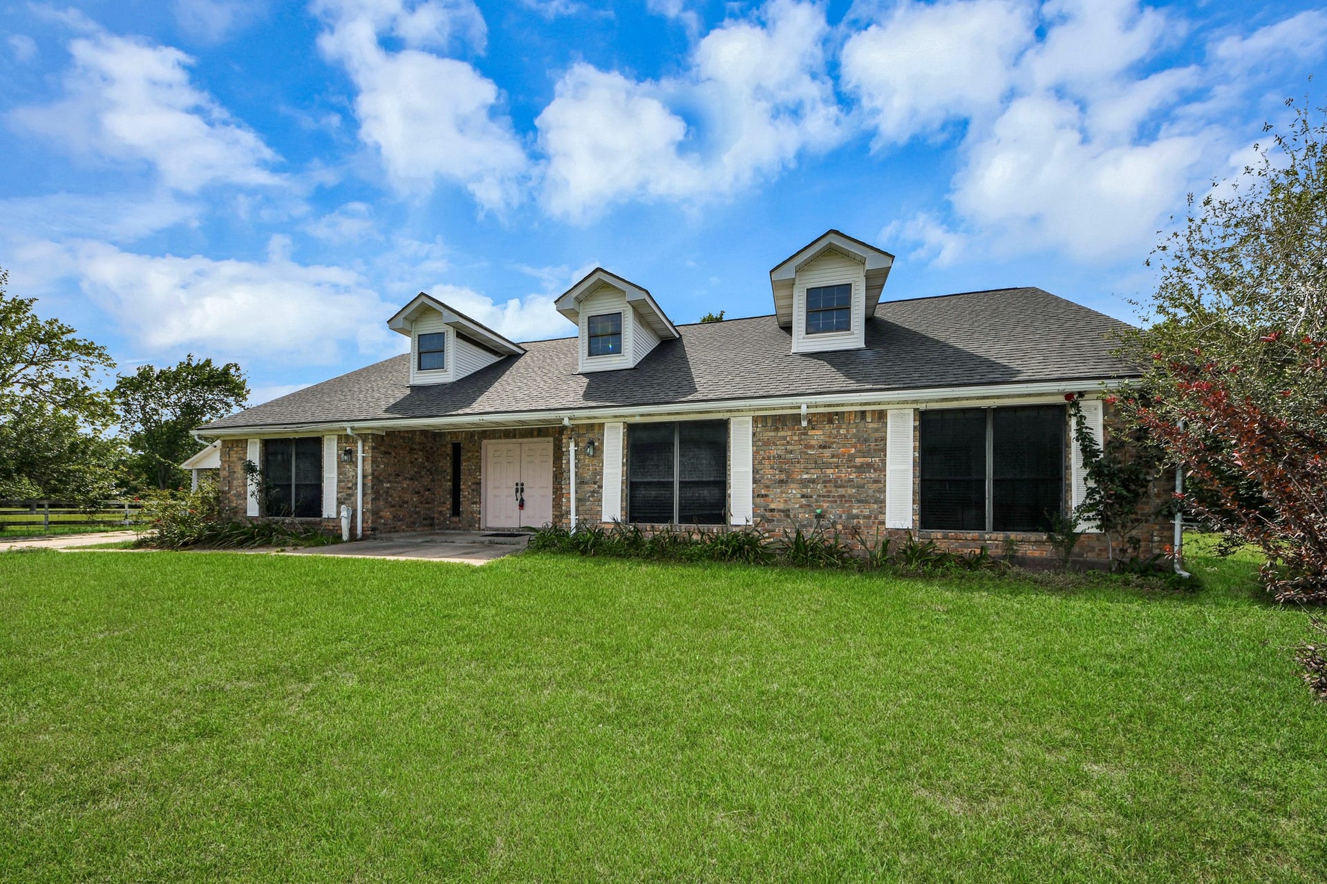12746 Roy Road, Pearland, TX 77581 This charming home features a classic brick exterior with three dormer windows, a spacious front porch, and a well-maintained lawn, set against a picturesque blue sky.