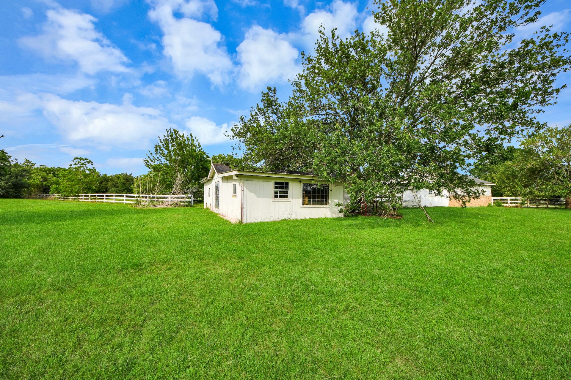 12746 Roy Road, Pearland, TX 77581 This photo features a charming single-story house surrounded by a spacious, lush green yard. It's set in a peaceful, rural area with a beautiful blue sky and scattered clouds, offering plenty of privacy and outdoor space.