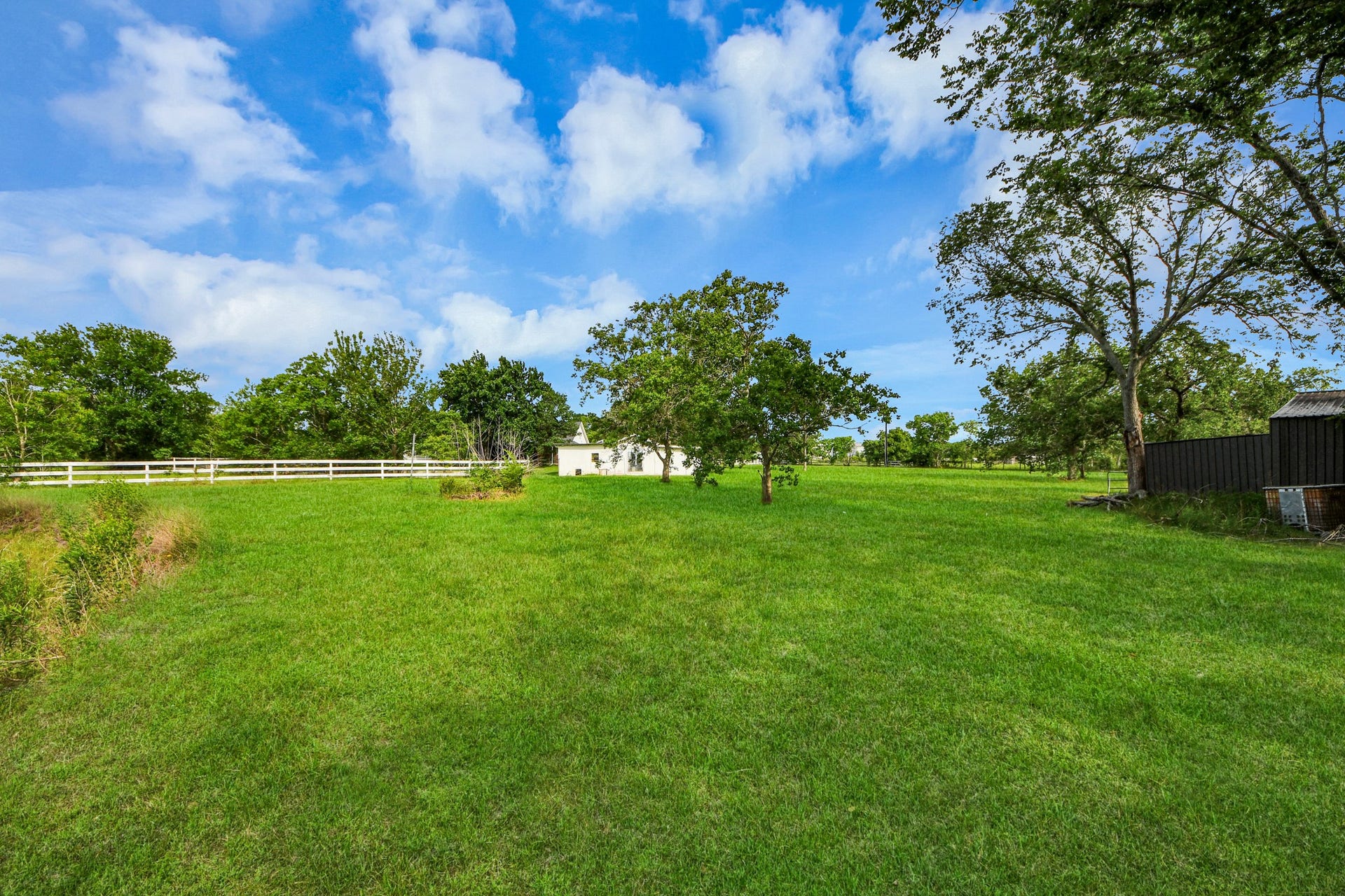 12746 Roy Road, Pearland, TX 77581 Expansive green lawn with mature trees, a small outbuilding, and a white fence, offering a serene, spacious outdoor setting perfect for relaxation or gardening.