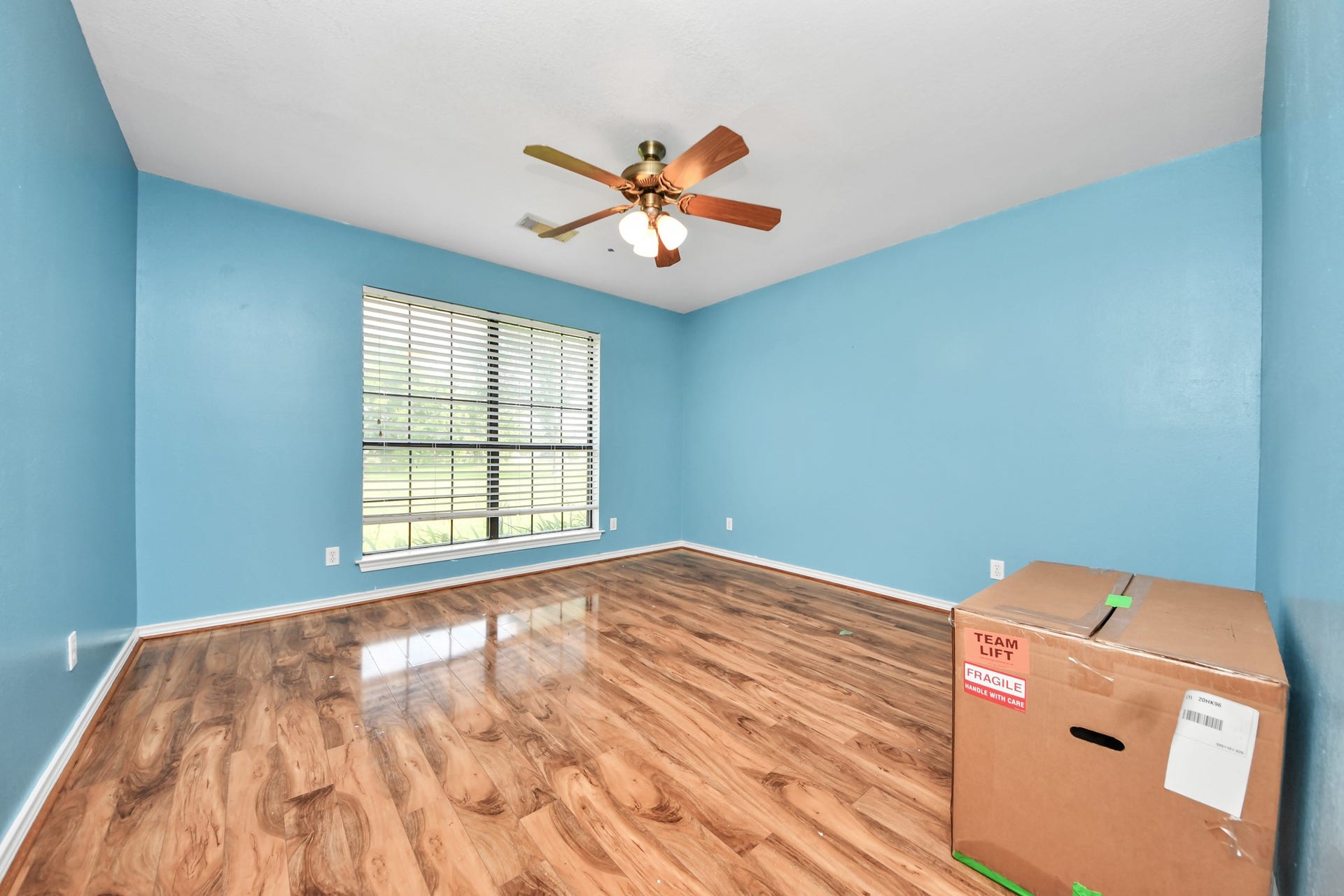 12746 Roy Road, Pearland, TX 77581 This room features bright blue walls, wood laminate flooring, and a ceiling fan with lights. A large window lets in ample natural light, creating a welcoming atmosphere.
