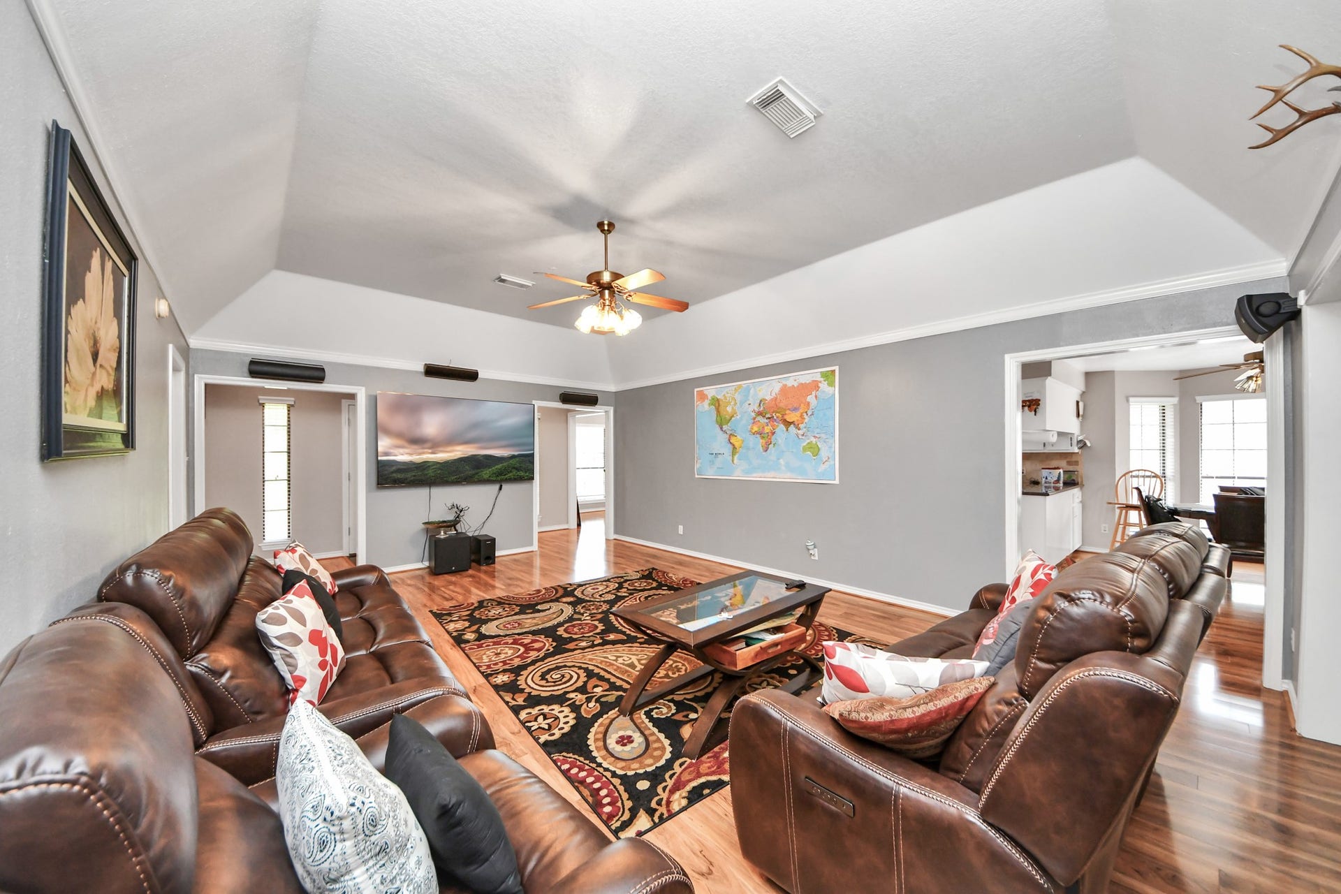 12746 Roy Road, Pearland, TX 77581 Spacious living room with vaulted ceilings, featuring leather seating, hardwood floors, and a ceiling fan. The room has large wall art, ample natural light, and opens into a cozy dining area and kitchen.