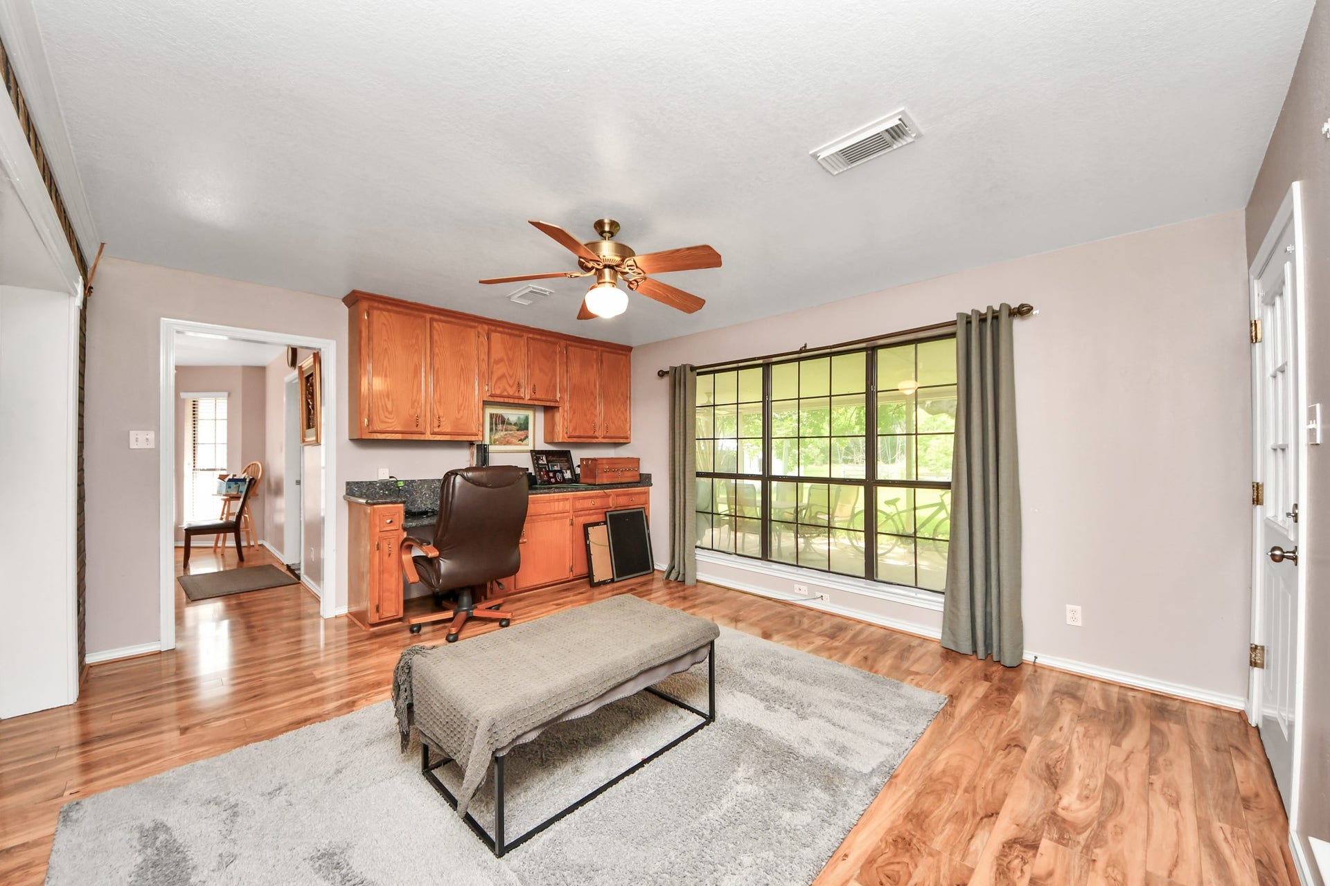 12746 Roy Road, Pearland, TX 77581 This room features a spacious, bright area with large windows and wooden flooring. It includes a built-in desk with cabinetry, a ceiling fan, and neutral-toned walls, creating a cozy and functional space.