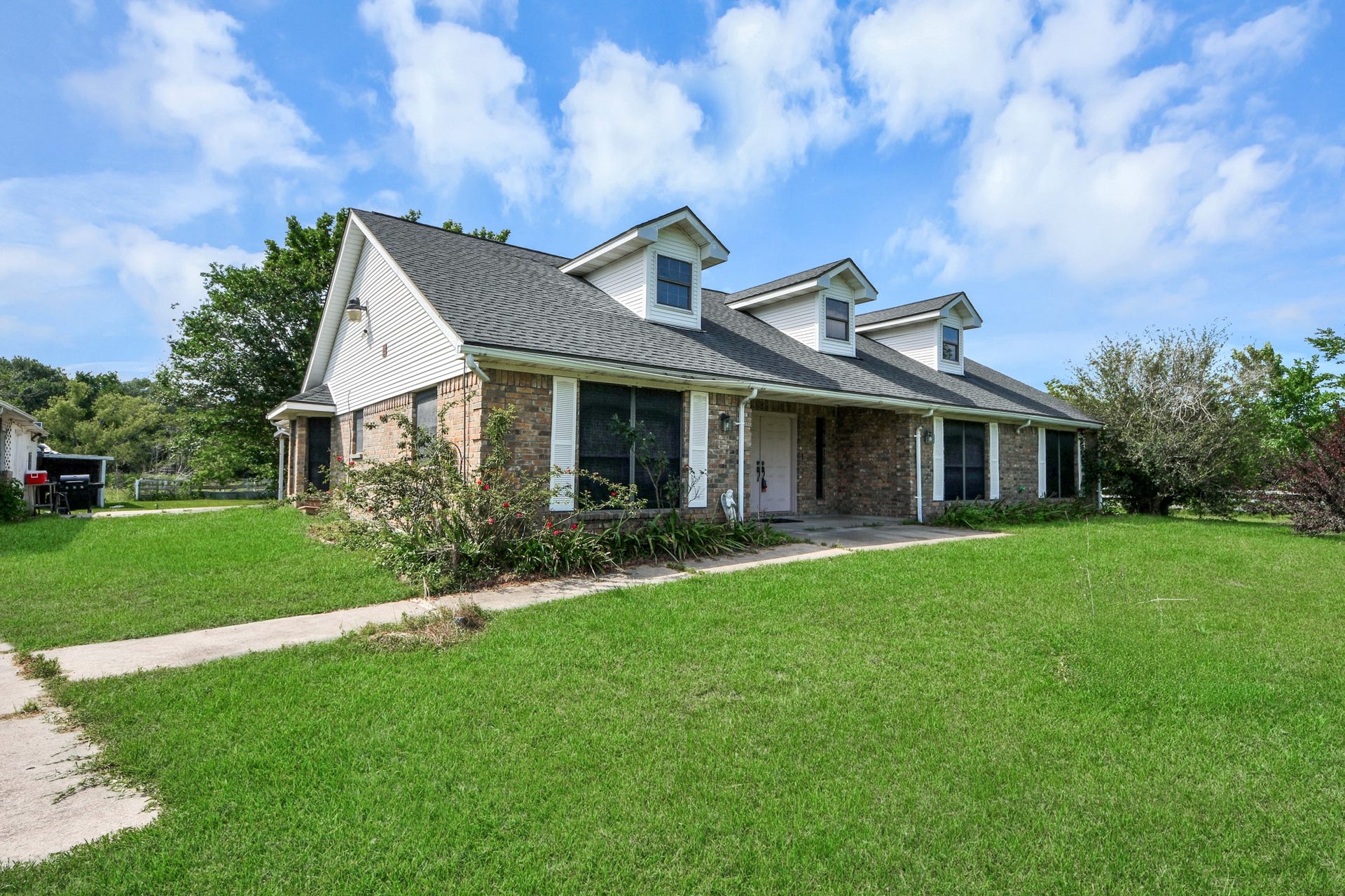 12746 Roy Road, Pearland, TX 77581 Charming single-story brick home with a spacious front yard and covered porch. Features dormer windows and a well-maintained lawn, offering a welcoming curb appeal.
