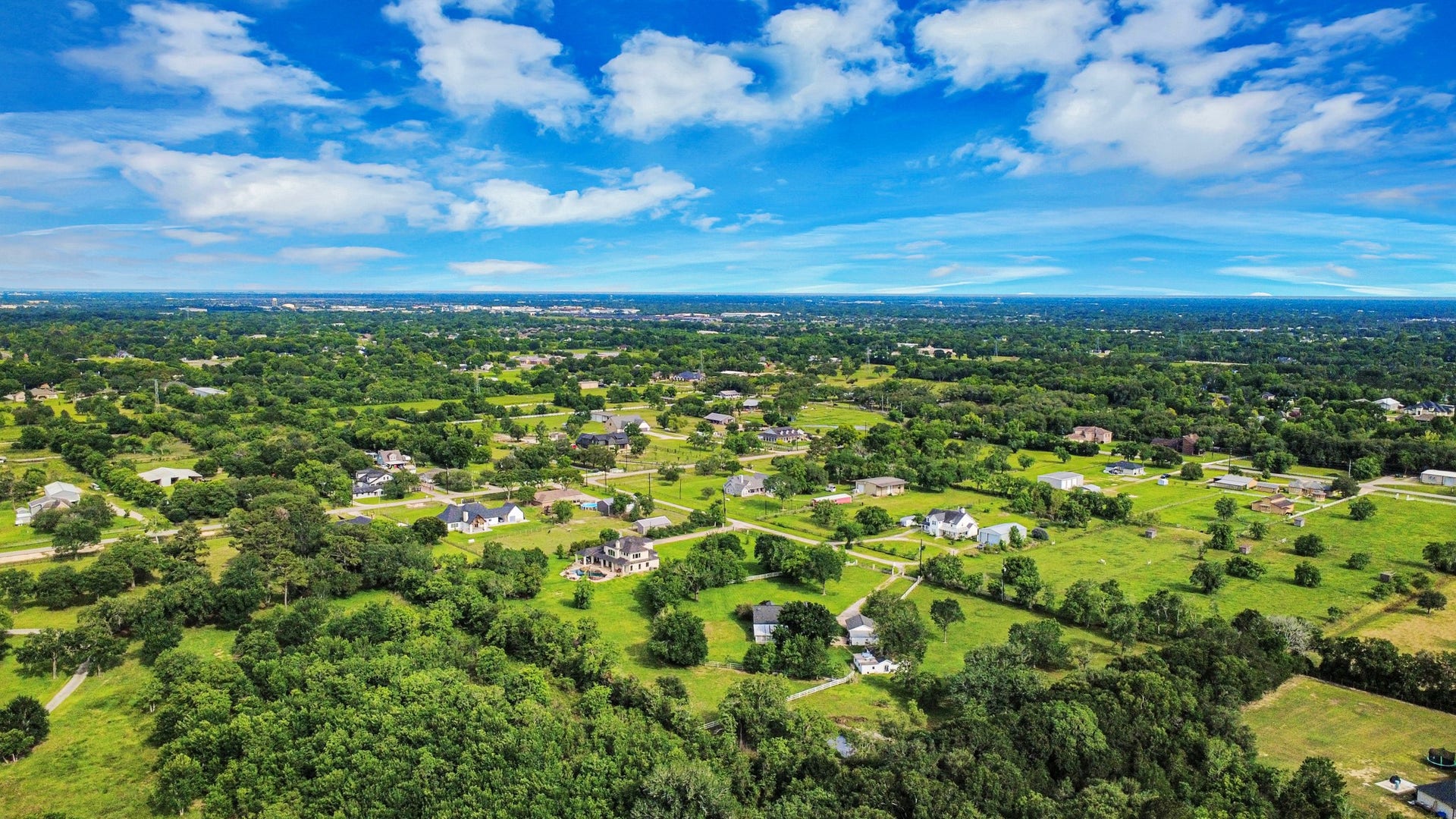 12746 Roy Road, Pearland, TX 77581 This aerial photo showcases a spacious, semi-rural neighborhood with scattered homes surrounded by lush greenery and open fields. The area offers a tranquil, expansive environment with clear blue skies and a sense of privacy, ideal for those seeking a peaceful lifestyle.