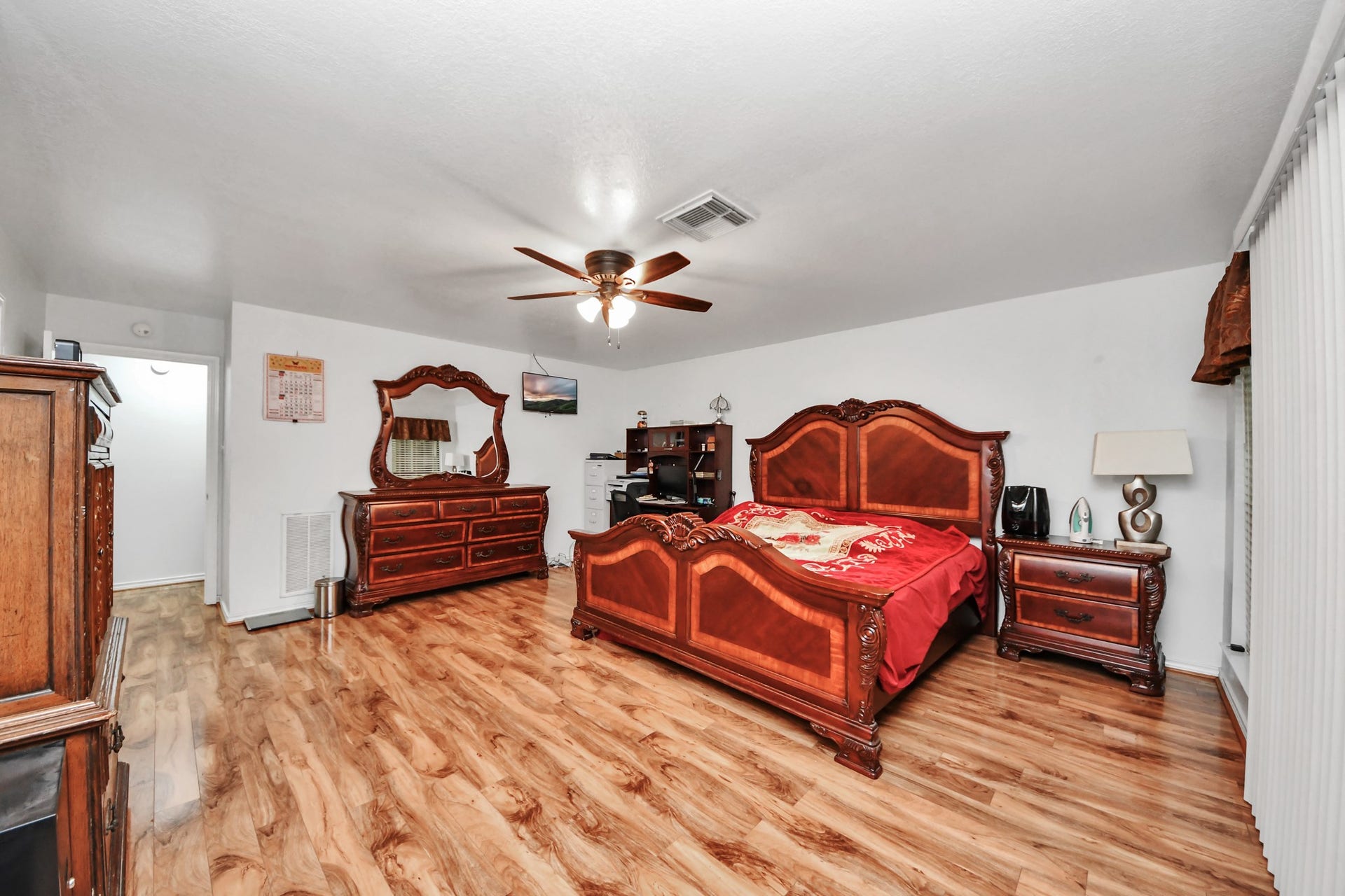 12746 Roy Road, Pearland, TX 77581 Spacious bedroom with elegant wood furniture, including a large bed, dresser, and nightstand. Features wood flooring, a ceiling fan, and ample natural light from sliding glass doors.