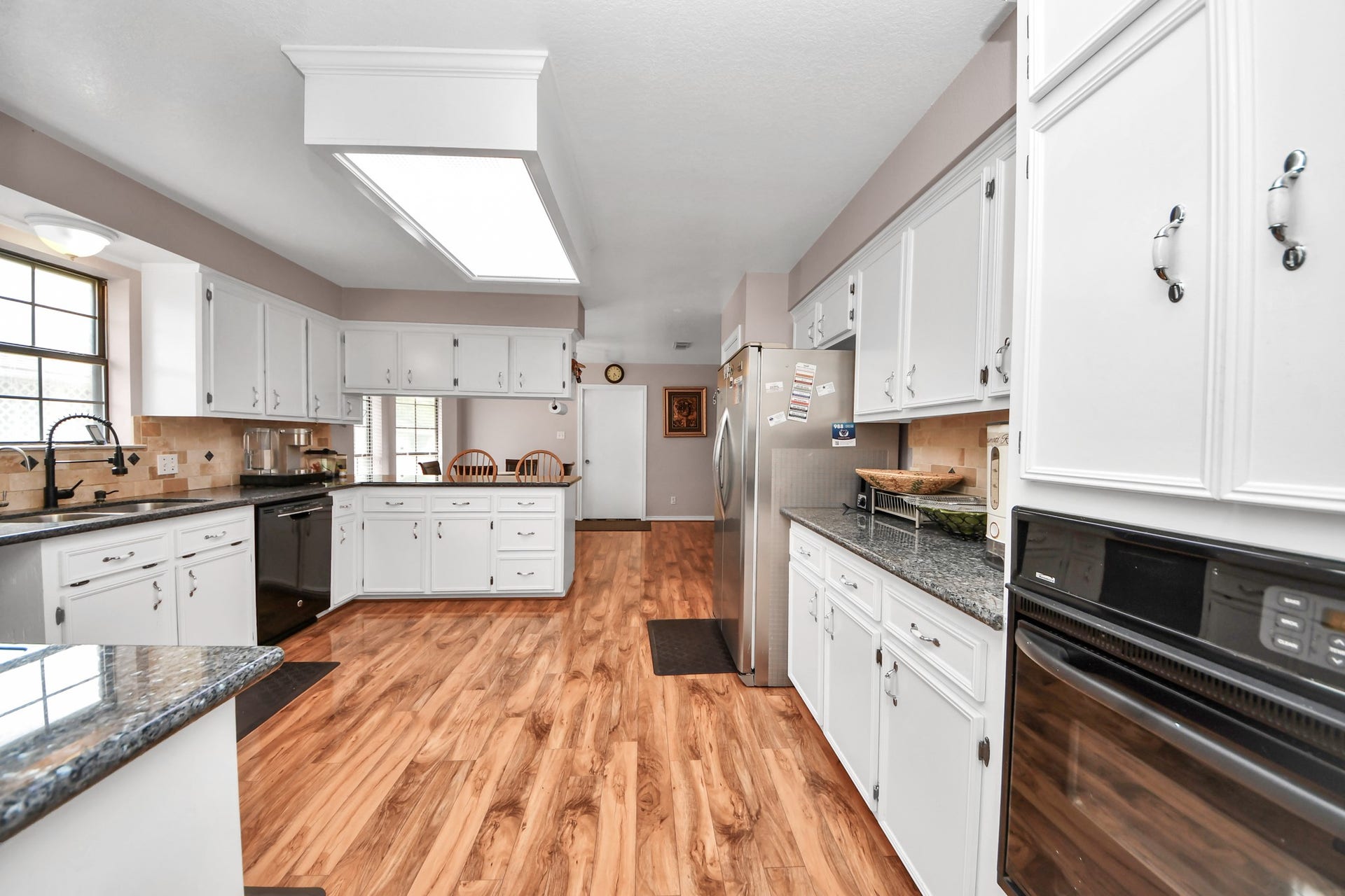 12746 Roy Road, Pearland, TX 77581 Spacious kitchen with white cabinets, granite countertops, and wood flooring. It features modern appliances, ample natural light, and a cozy dining nook.