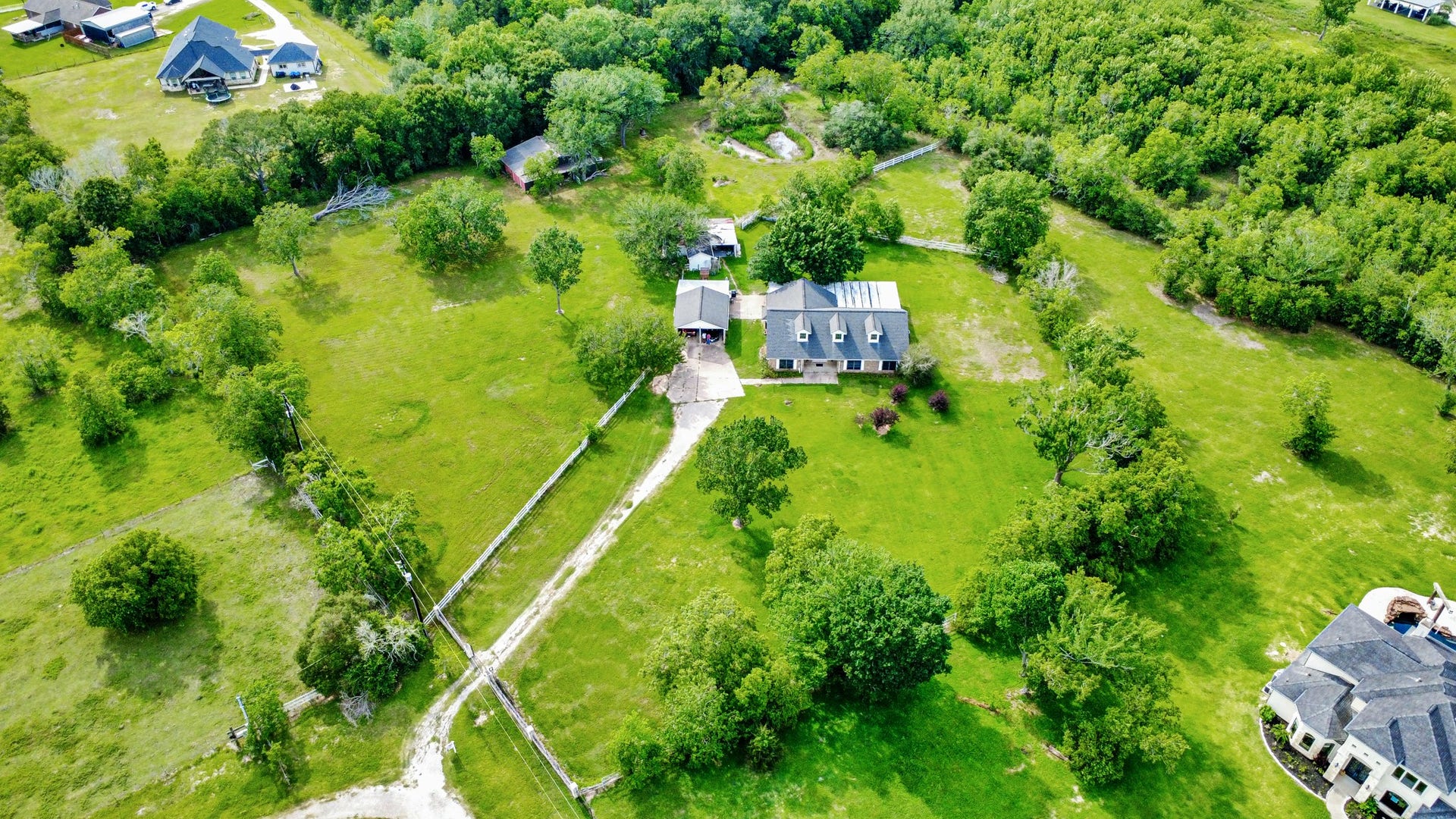 12746 Roy Road, Pearland, TX 77581 This aerial photo showcases a spacious rural property with a large house surrounded by lush greenery and trees. The home has a long driveway and is set on a sizable plot of land, offering privacy and a serene environment.