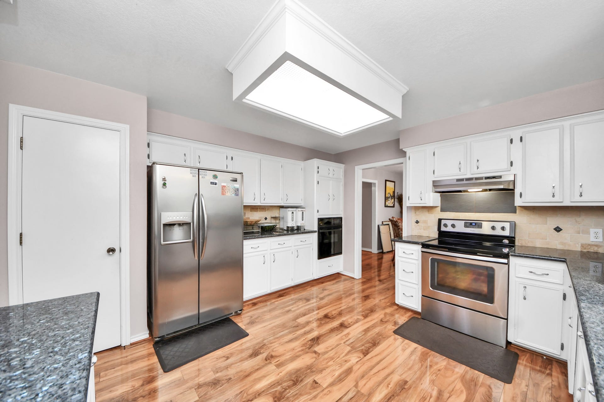 12746 Roy Road, Pearland, TX 77581 This kitchen features modern stainless steel appliances, white cabinetry, and sleek stone countertops. It has a warm, inviting atmosphere with hardwood floors and ample lighting.