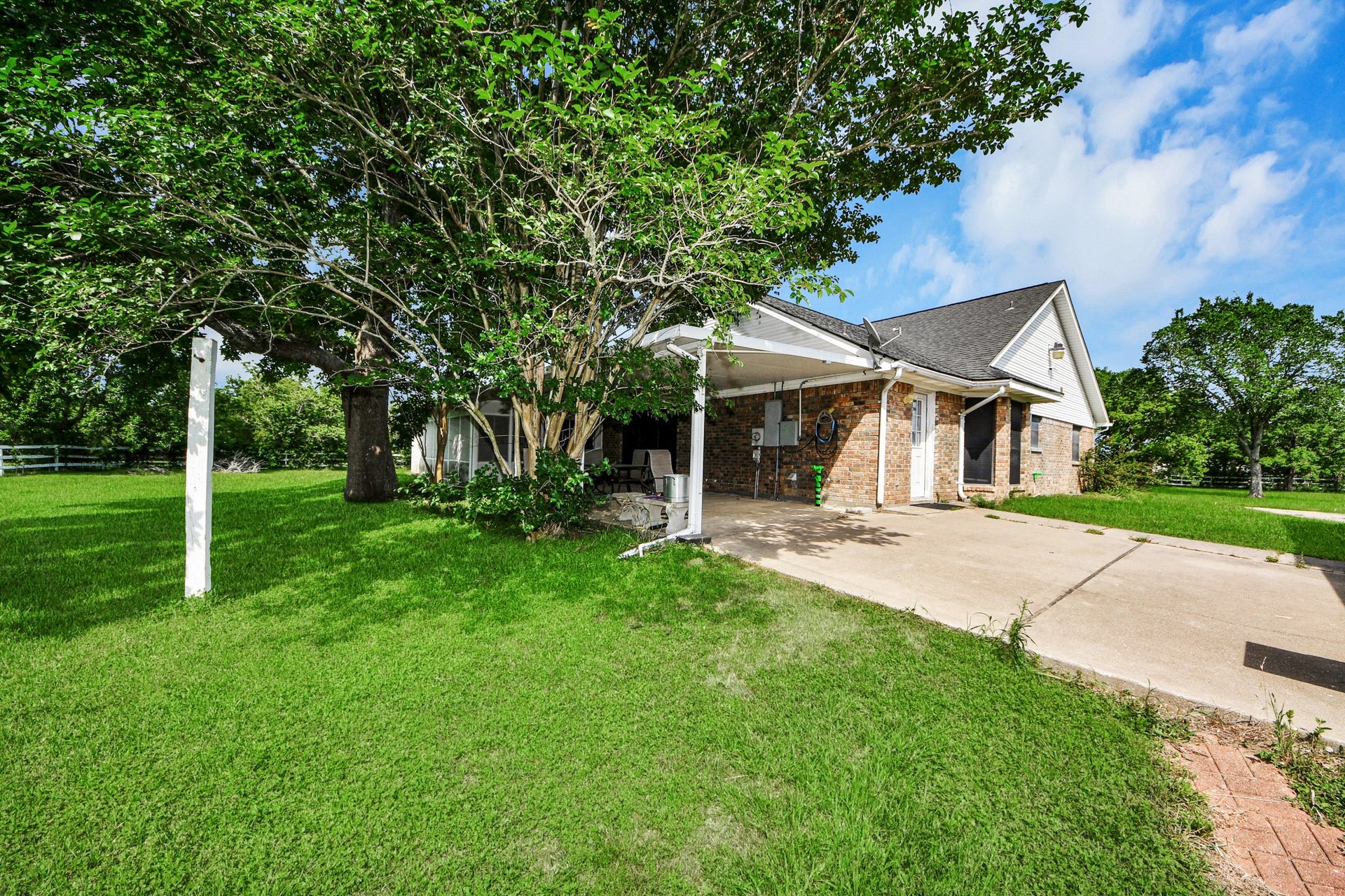 12746 Roy Road, Pearland, TX 77581 Charming brick house with a carport, surrounded by lush greenery and mature trees. The spacious yard offers ample space, perfect for outdoor activities or gardening.