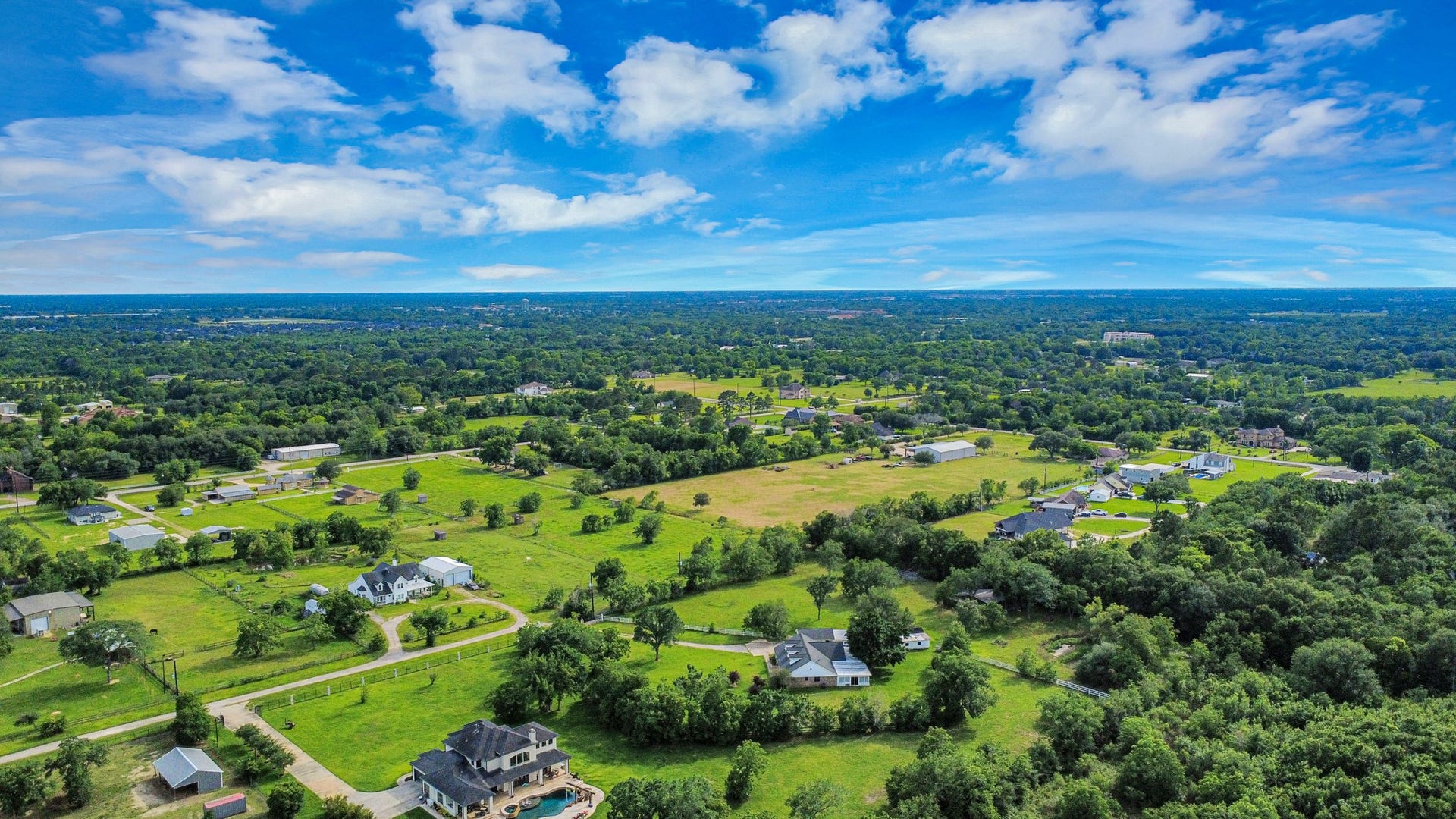 12746 Roy Road, Pearland, TX 77581 This aerial photo showcases a spacious rural area with scattered homes, lush greenery, and open fields under a bright blue sky, offering a peaceful and expansive setting ideal for privacy and nature lovers.