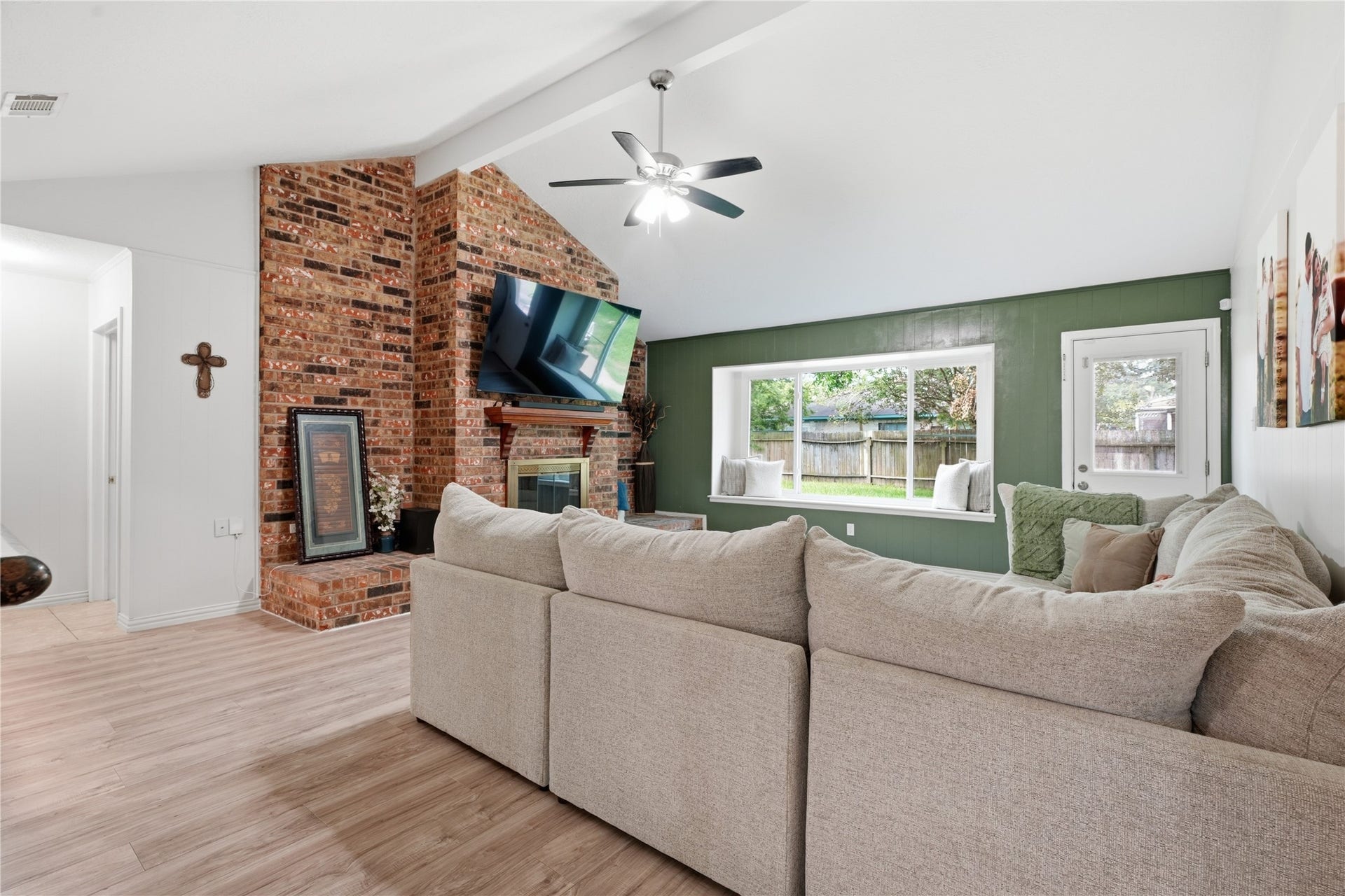 4850 Kentington Drive, Alvin, TX 77511 Bright, open living room featuring vaulted ceilings, a brick fireplace, large picture window, and access to the backyard.