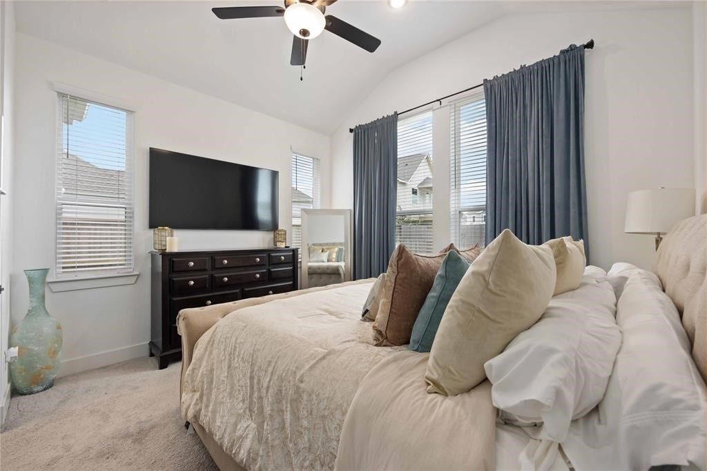 Virtually Staged - This bedroom features a cozy, carpeted space with a ceiling fan, natural light from large windows with blue curtains, and a stylish setup including a TV, dresser, and plush bedding.