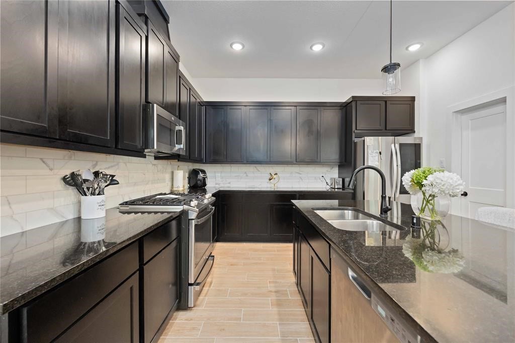 Virtually Staged - This modern kitchen features sleek dark cabinetry, stainless steel appliances, and a stylish tile backsplash. The spacious layout includes a large island with a dual sink and ample counter space, perfect for cooking and entertaining.