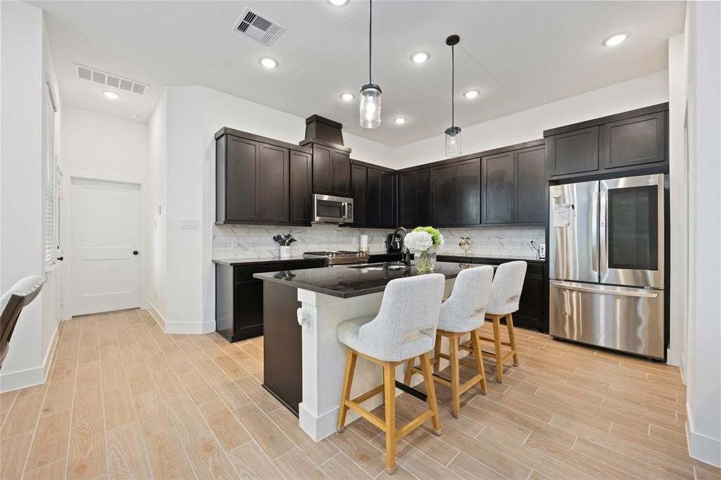 Virtually Staged - This modern kitchen features sleek dark cabinetry, stainless steel appliances, and a spacious island with seating for four. The light wood flooring and recessed lighting create a bright, inviting space ideal for cooking and entertaining.