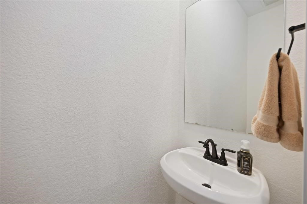 Virtually Staged - This photo shows a compact, well-lit powder room featuring a white pedestal sink with a black faucet, a wall-mounted mirror, and a towel holder with beige towels.