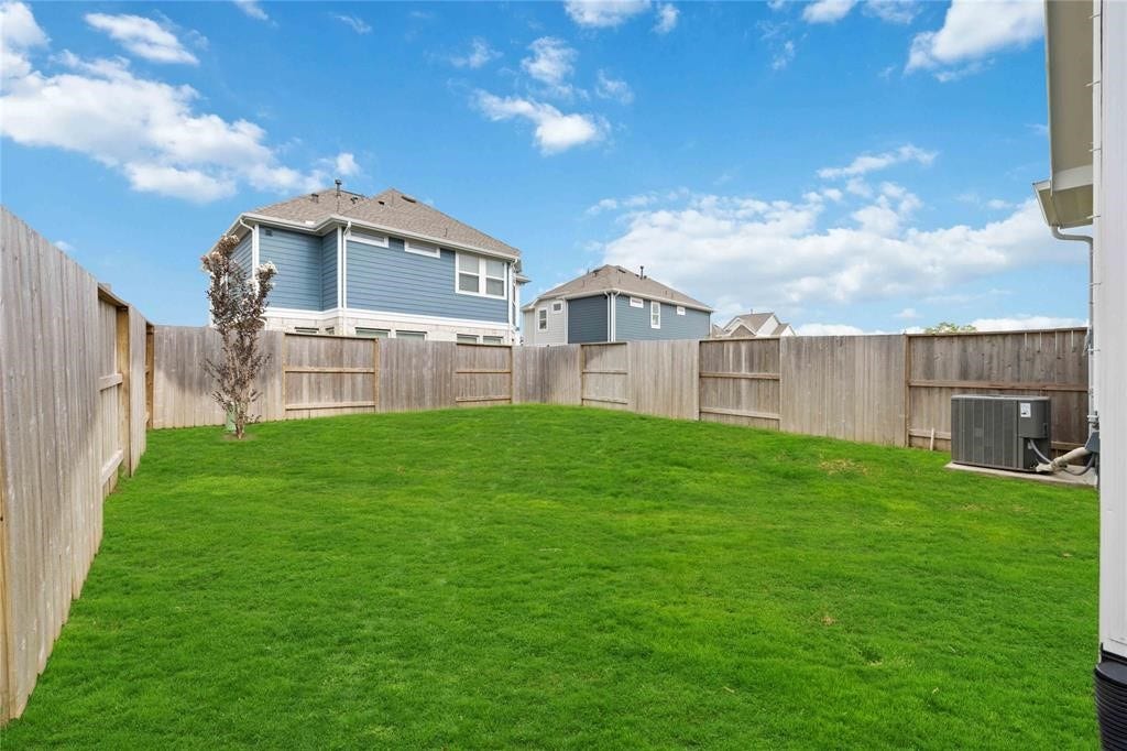 Virtually Staged - Spacious backyard with lush green grass, enclosed by a wooden fence, offering privacy and ideal for outdoor activities.