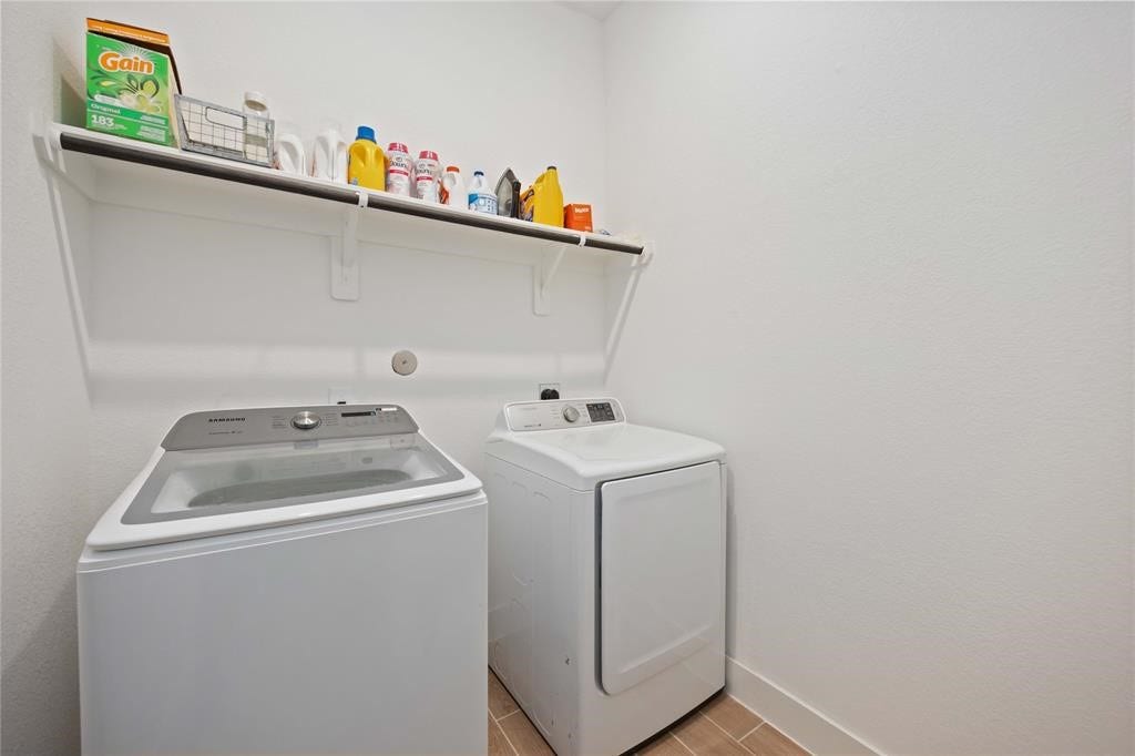 Virtually Staged - This photo shows a compact laundry room with a modern washer and dryer, a shelf above for storage, and clean, white walls.