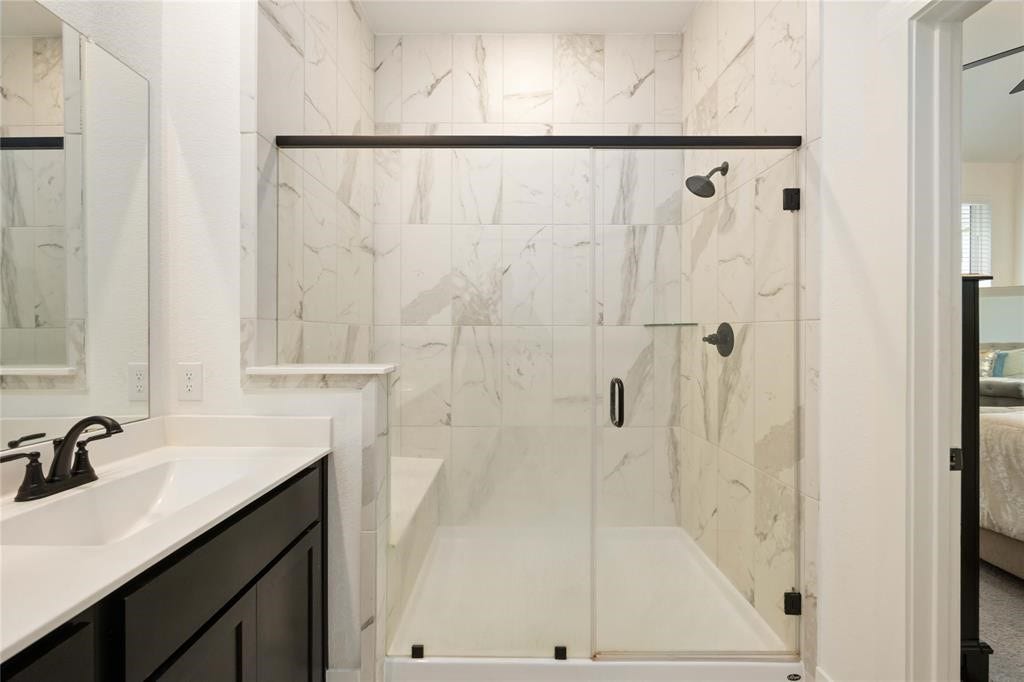 Virtually Staged - Modern bathroom featuring a spacious glass-enclosed shower with elegant marble tile, a sleek vanity with a black faucet, and an adjacent bedroom.