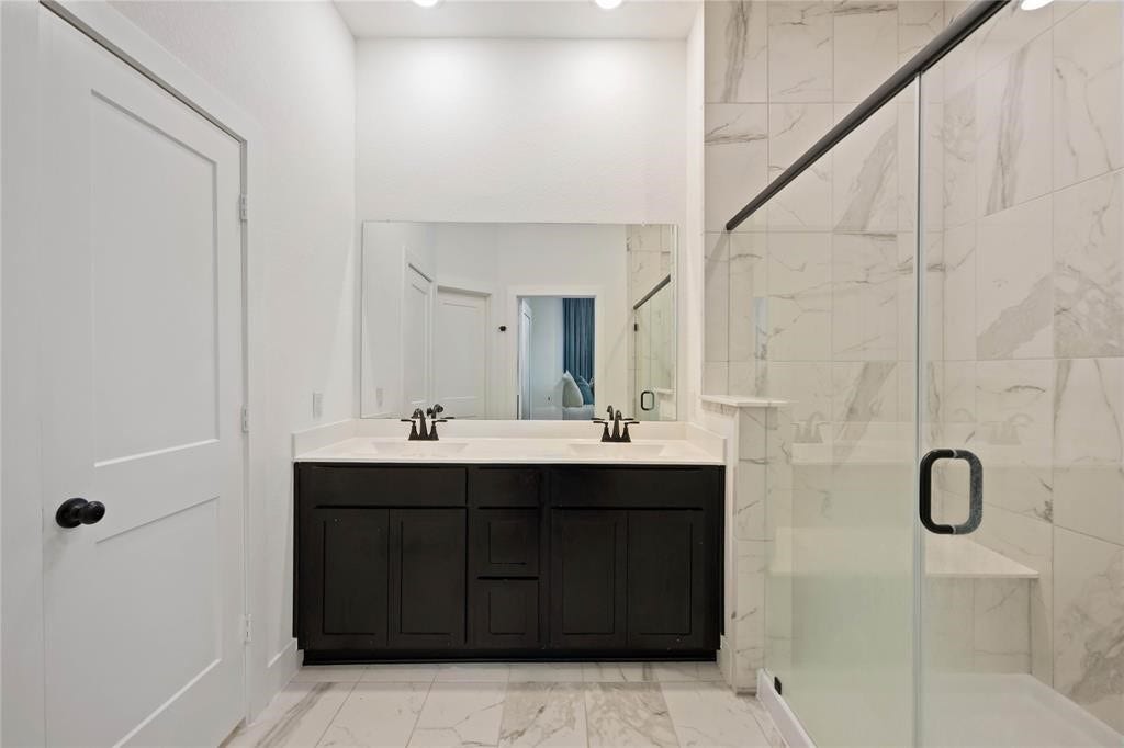 Virtually Staged - This bathroom features a modern design with a sleek double vanity, large mirror, and a spacious glass-enclosed shower. The white and gray marble tiles add a touch of elegance.